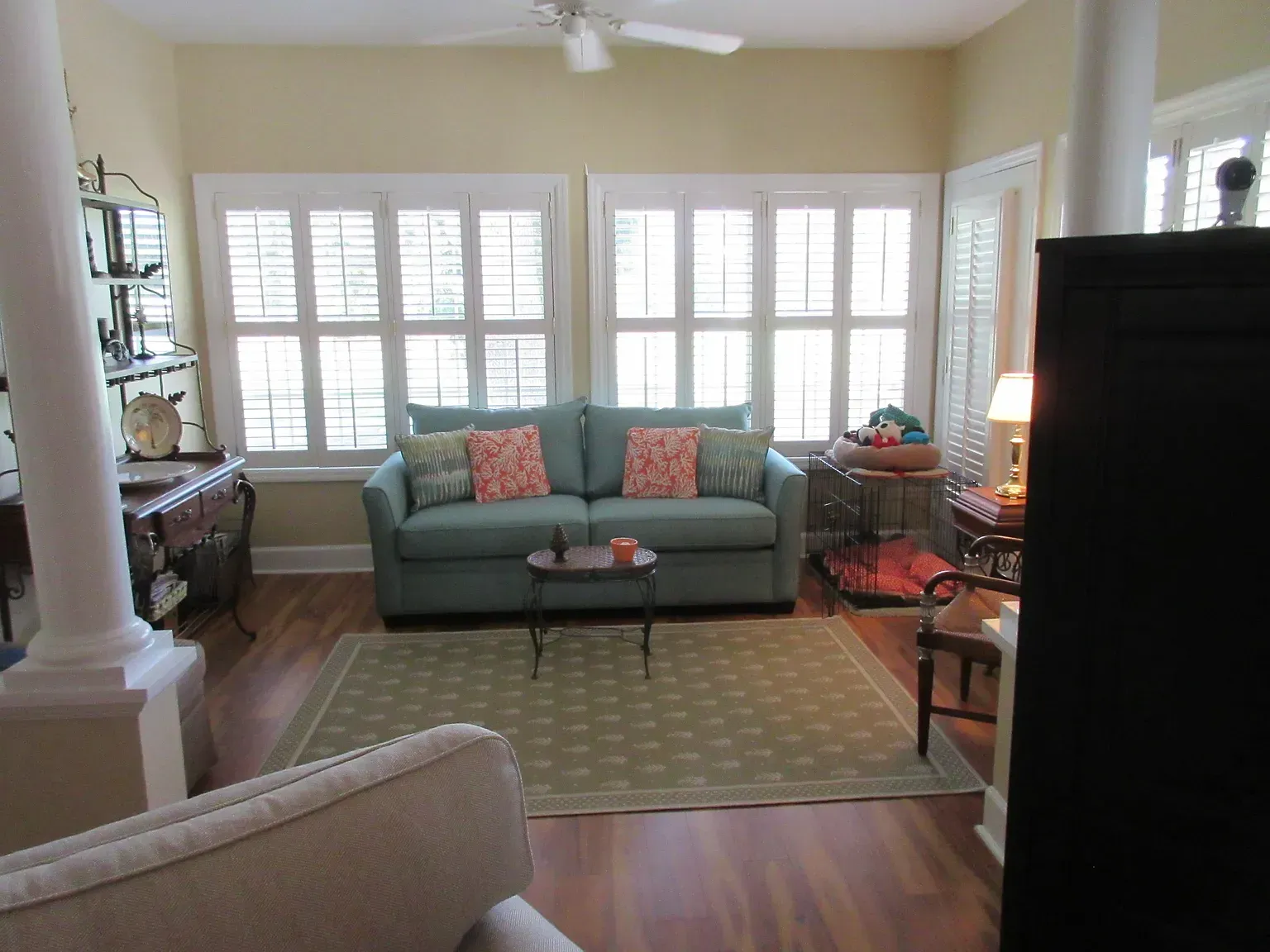 Living room with teal sofa, window shutters, and green rug.