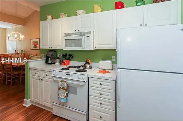 White kitchen with appliances, cabinets, and dining area in the background. Green walls, white countertops, and wood floors.