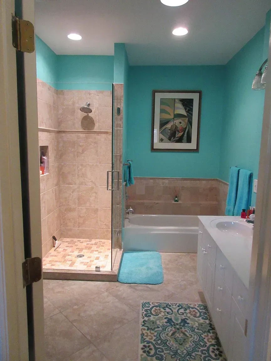 Bathroom with turquoise walls, beige tile shower, white tub, and a decorative rug.