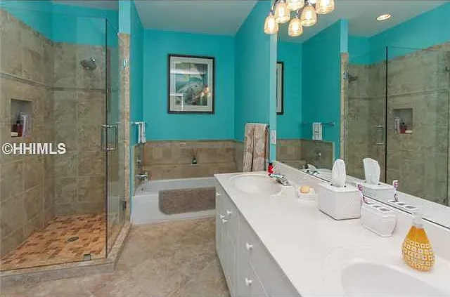 Bathroom with turquoise walls, beige tile, glass shower, double sinks, and a bathtub.