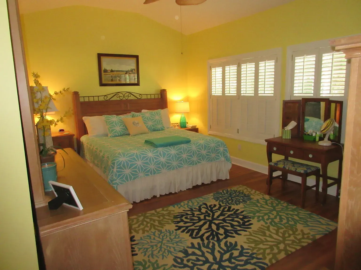 Bedroom with yellow walls, turquoise bedding, and a coral-patterned rug.