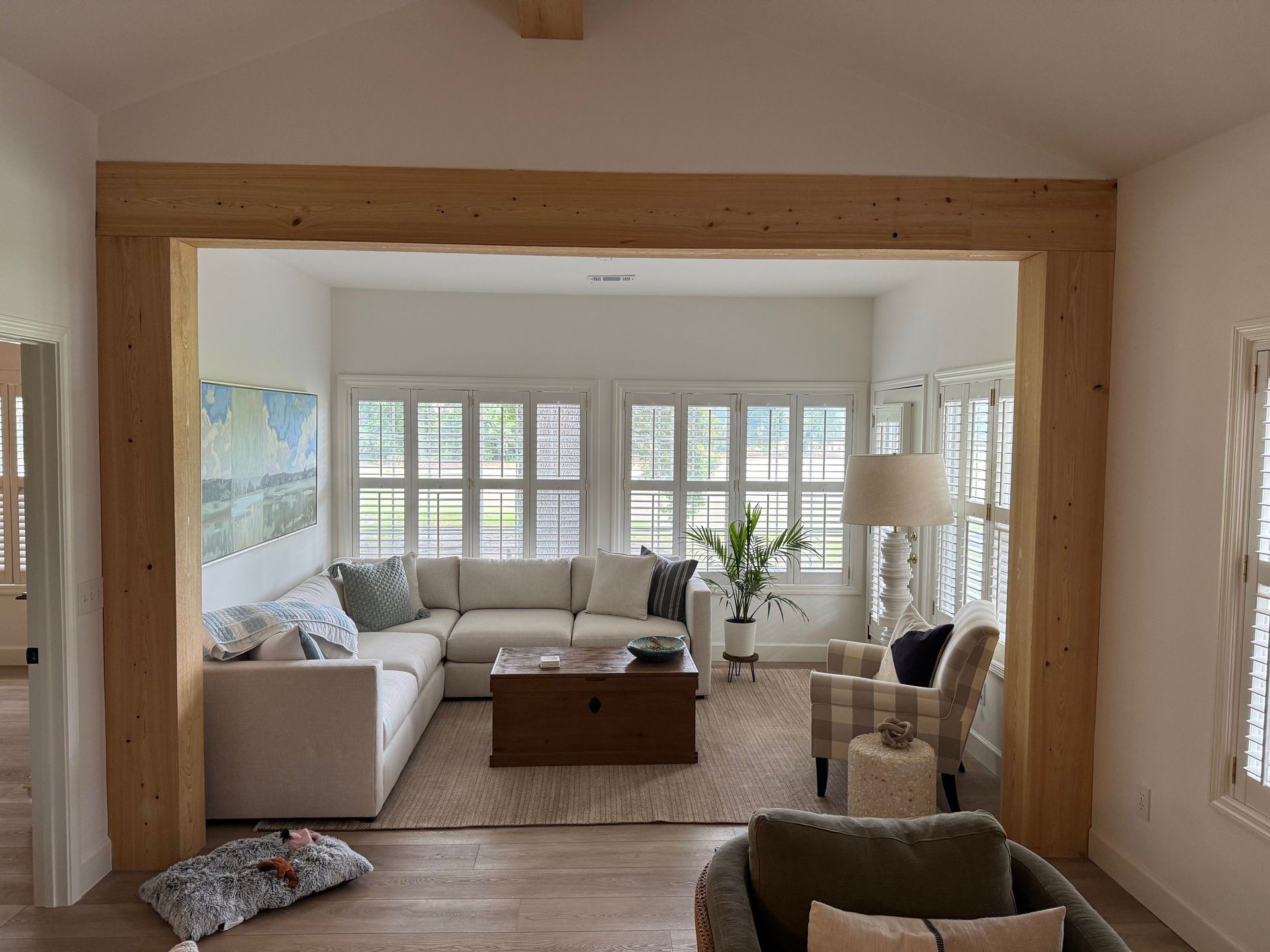 Open living area with light wood beams framing a seating area with a sectional sofa and armchairs.