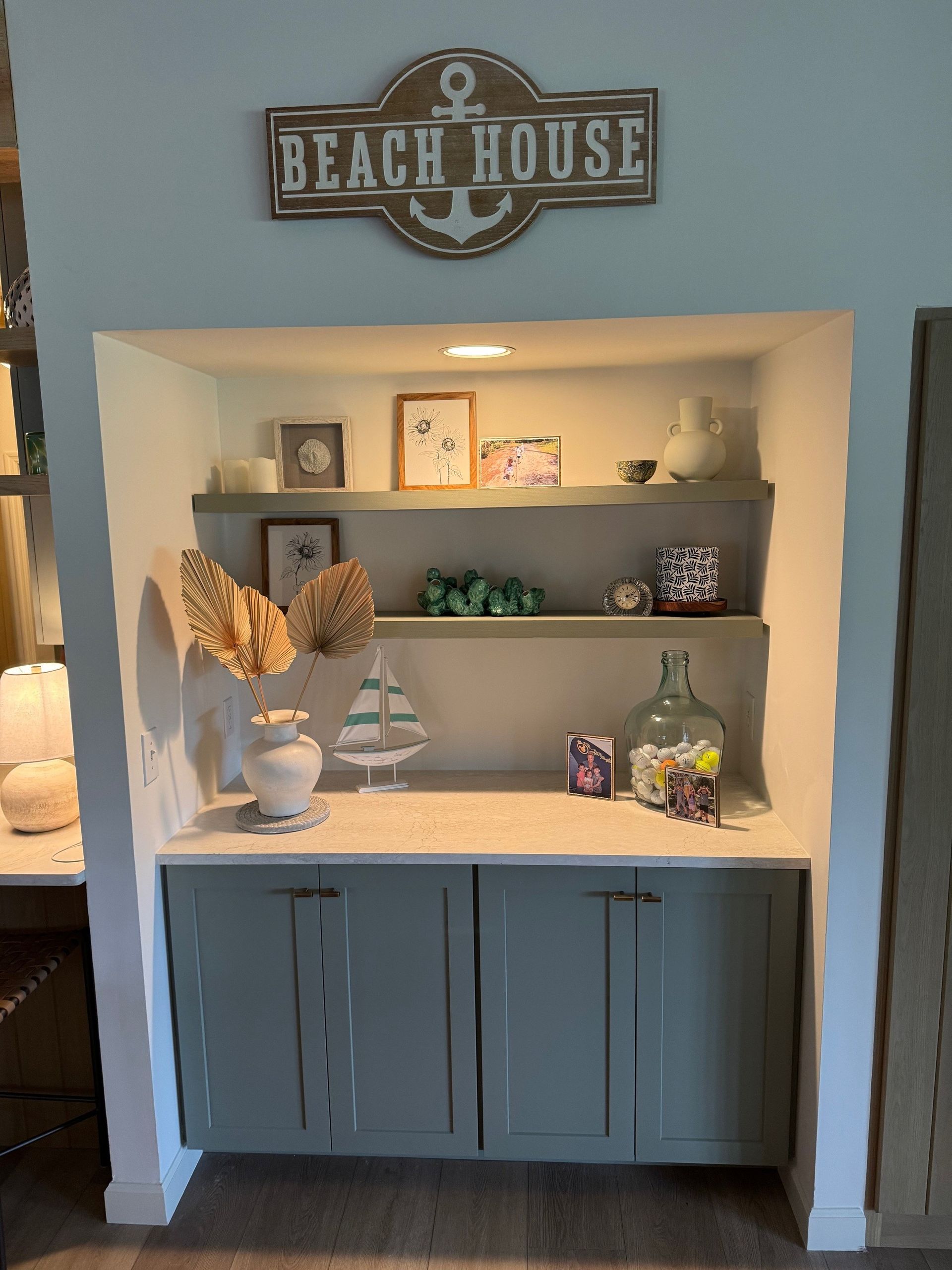 Built-in cabinet with open shelving, painted in a coastal theme. Displays include décor and a “Beach House” sign.