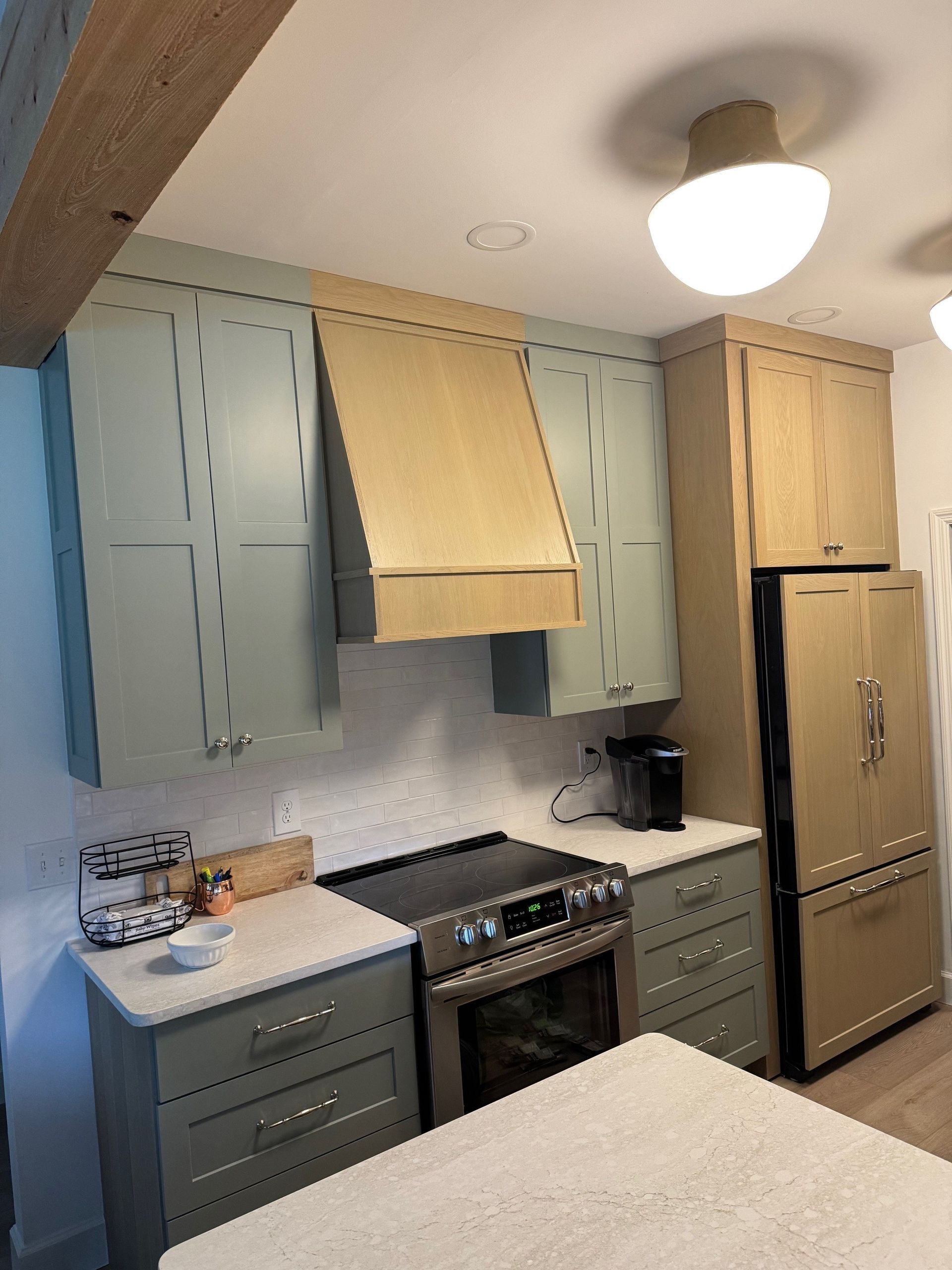 Kitchen with light green cabinets, stainless steel appliances, and beige refrigerator.