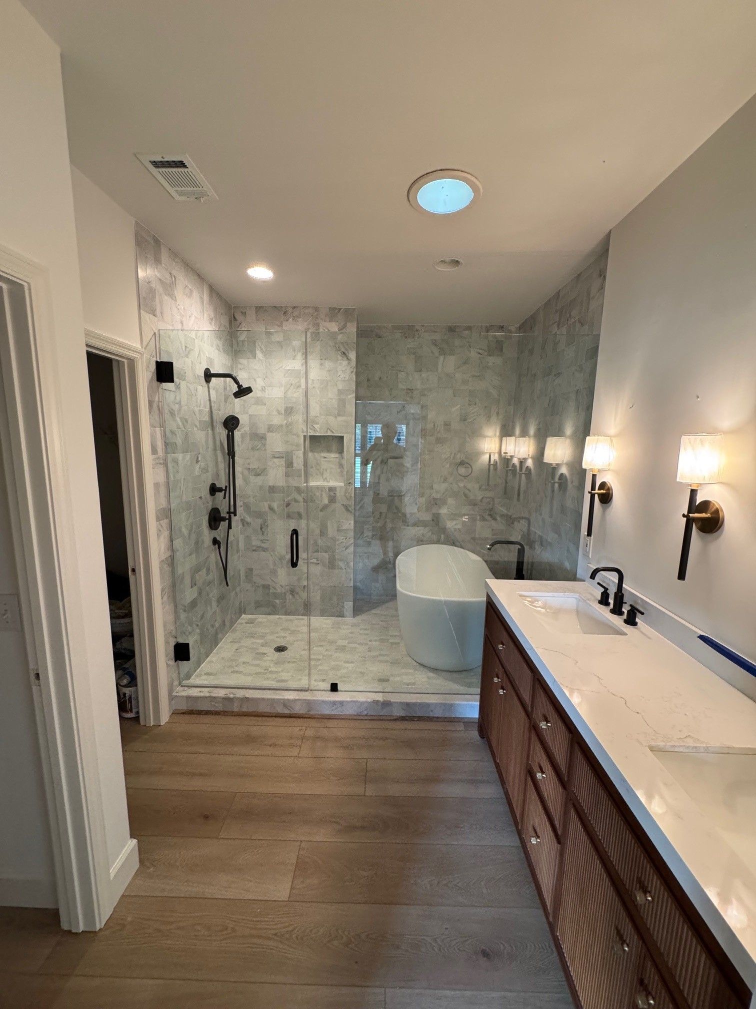 Modern bathroom with shower, tub, double vanity, and wood flooring. Light gray marble tile walls.