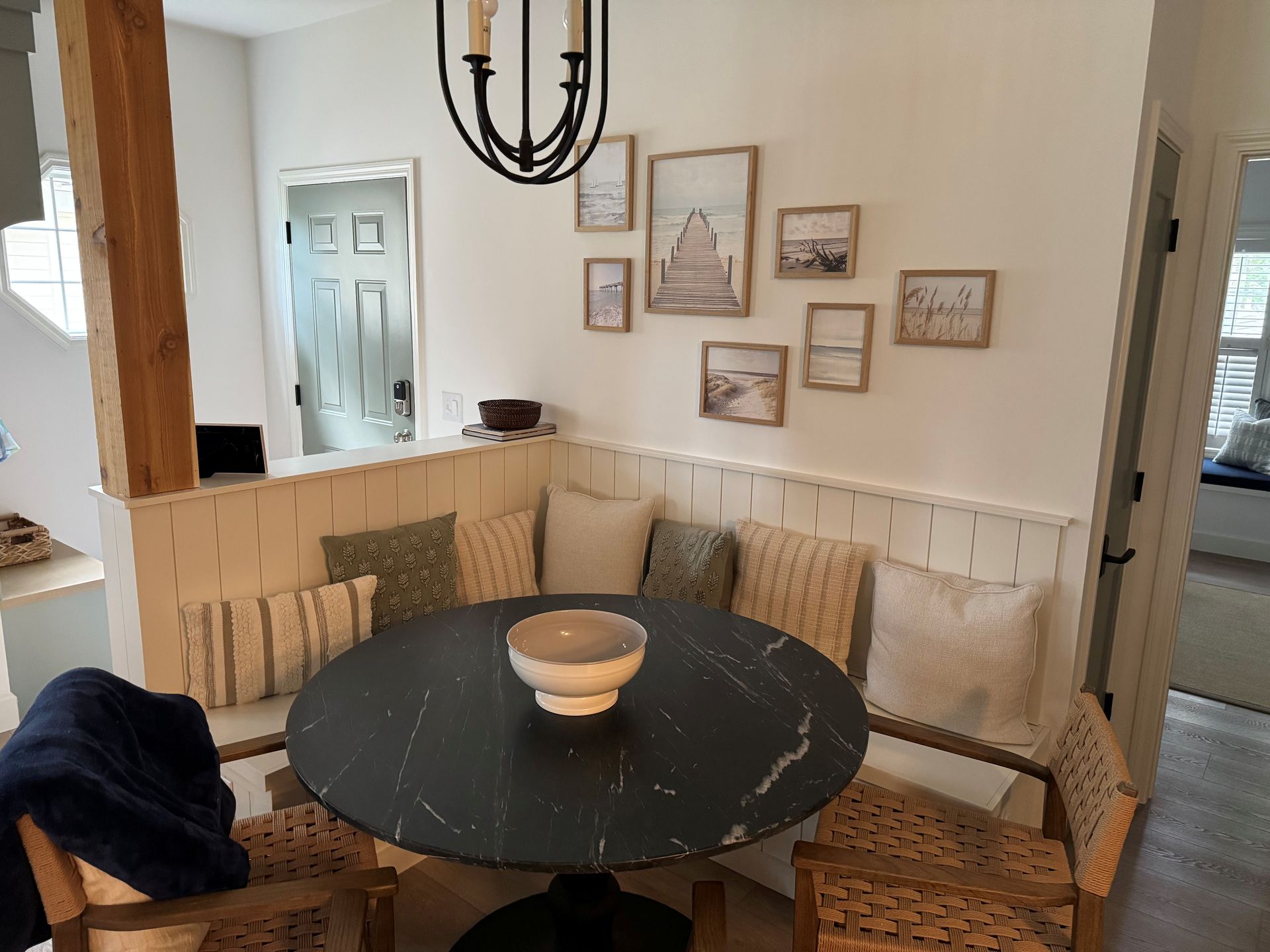 Cozy breakfast nook with round dark table, built-in bench seating, art, and chandelier.