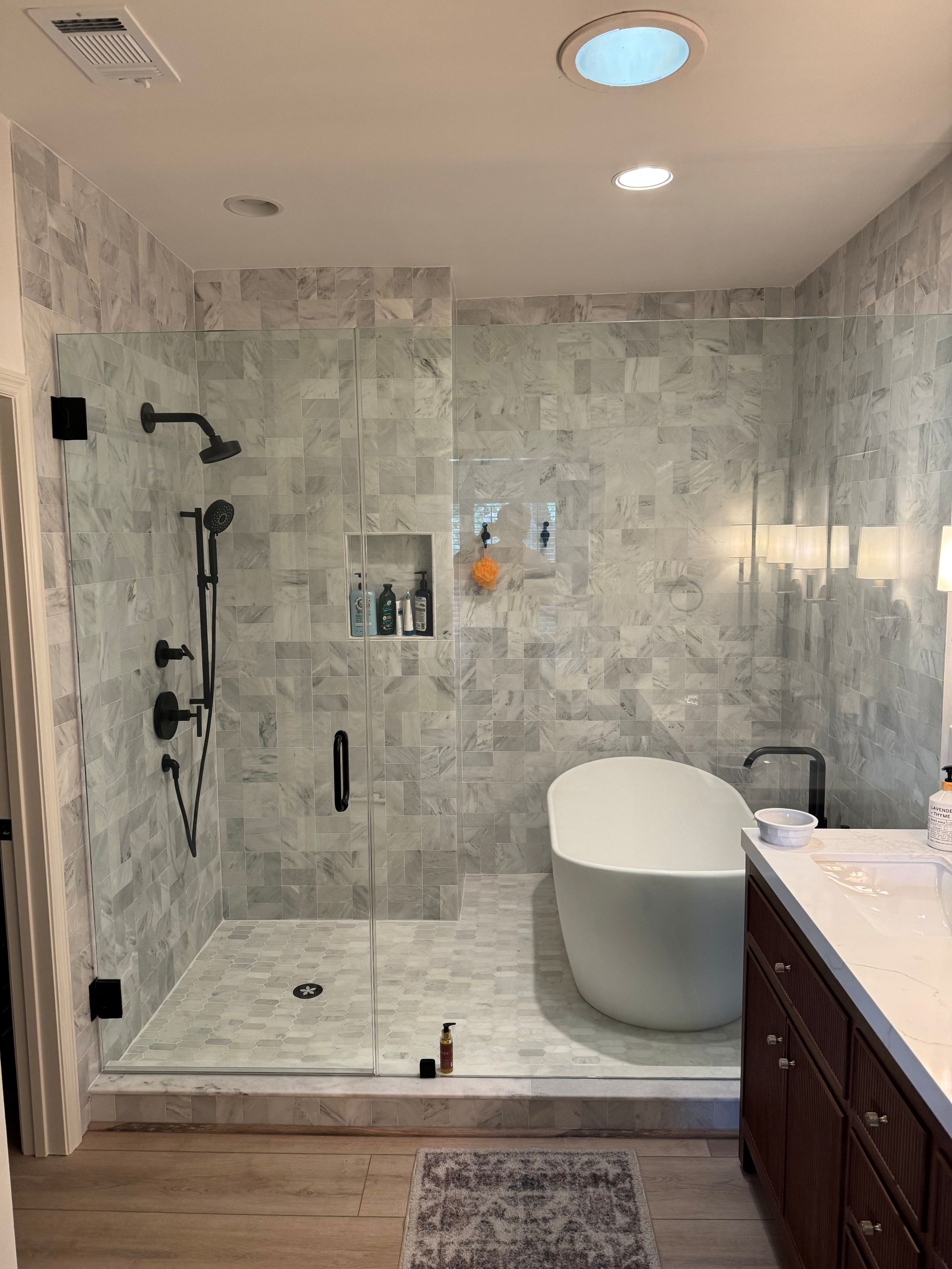 Bathroom with marble tile, glass shower, freestanding tub, and dark wood vanity.
