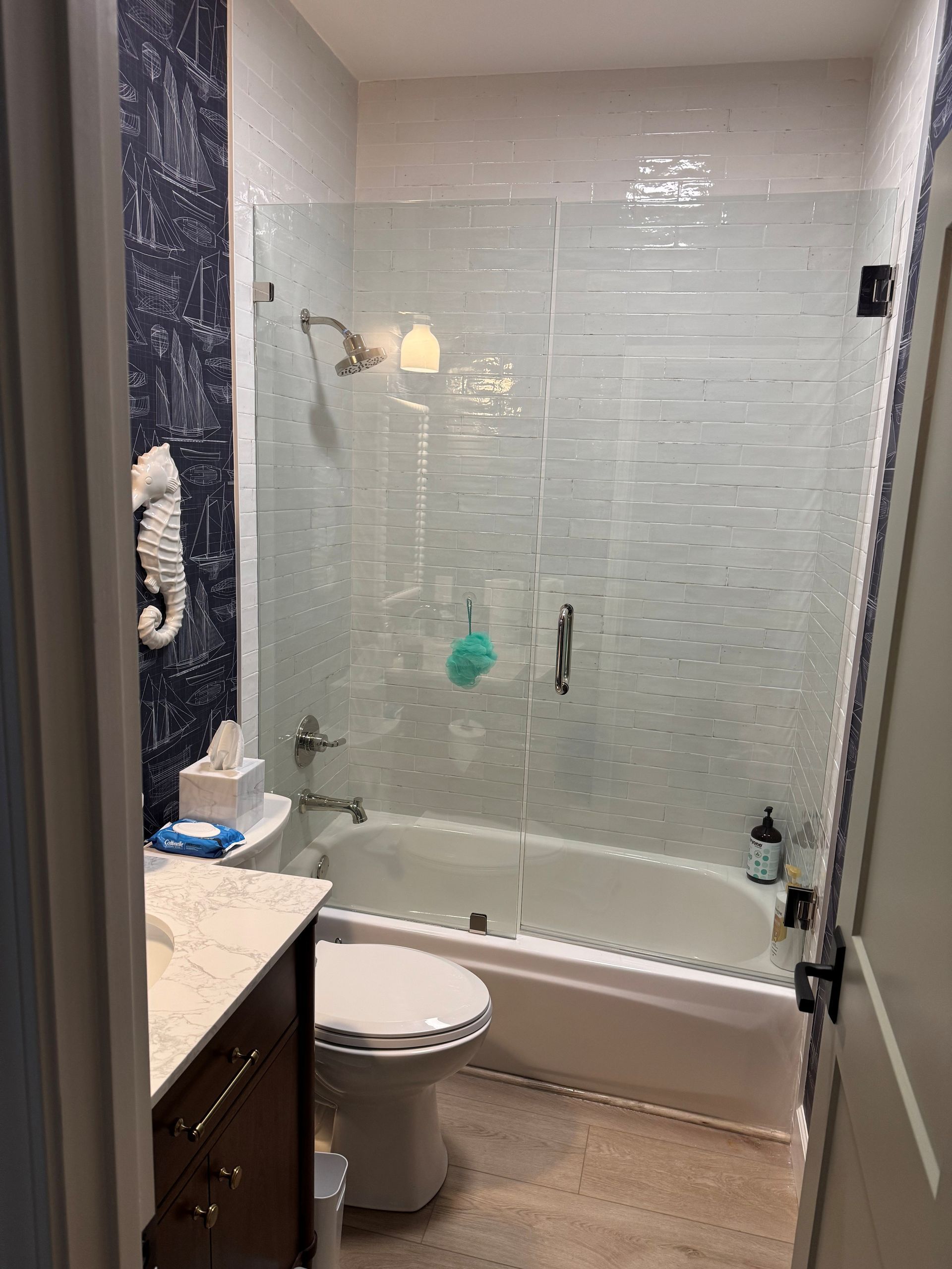 Bathroom with white tub, toilet, and glass shower door; blue and white tiled walls.