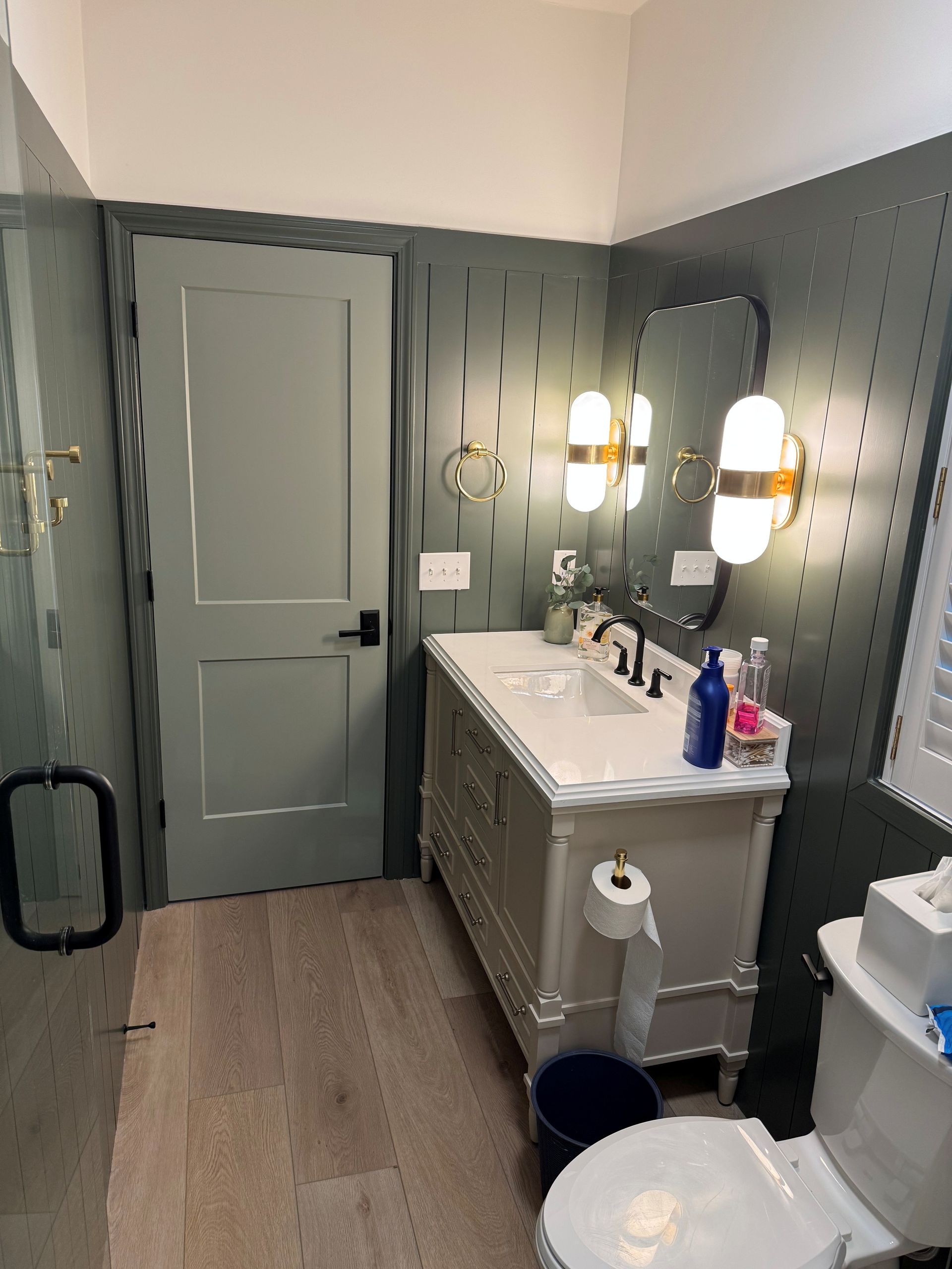Bathroom with gray door, vanity, and toilet. Gray textured wall with decorative lights and mirror.