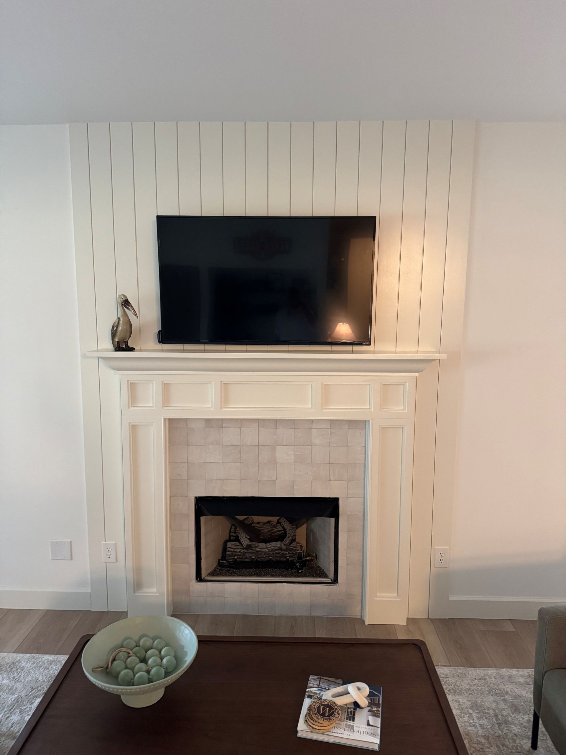 Fireplace with a mounted TV, white mantel, and wood paneling on the wall. A coffee table is in front.