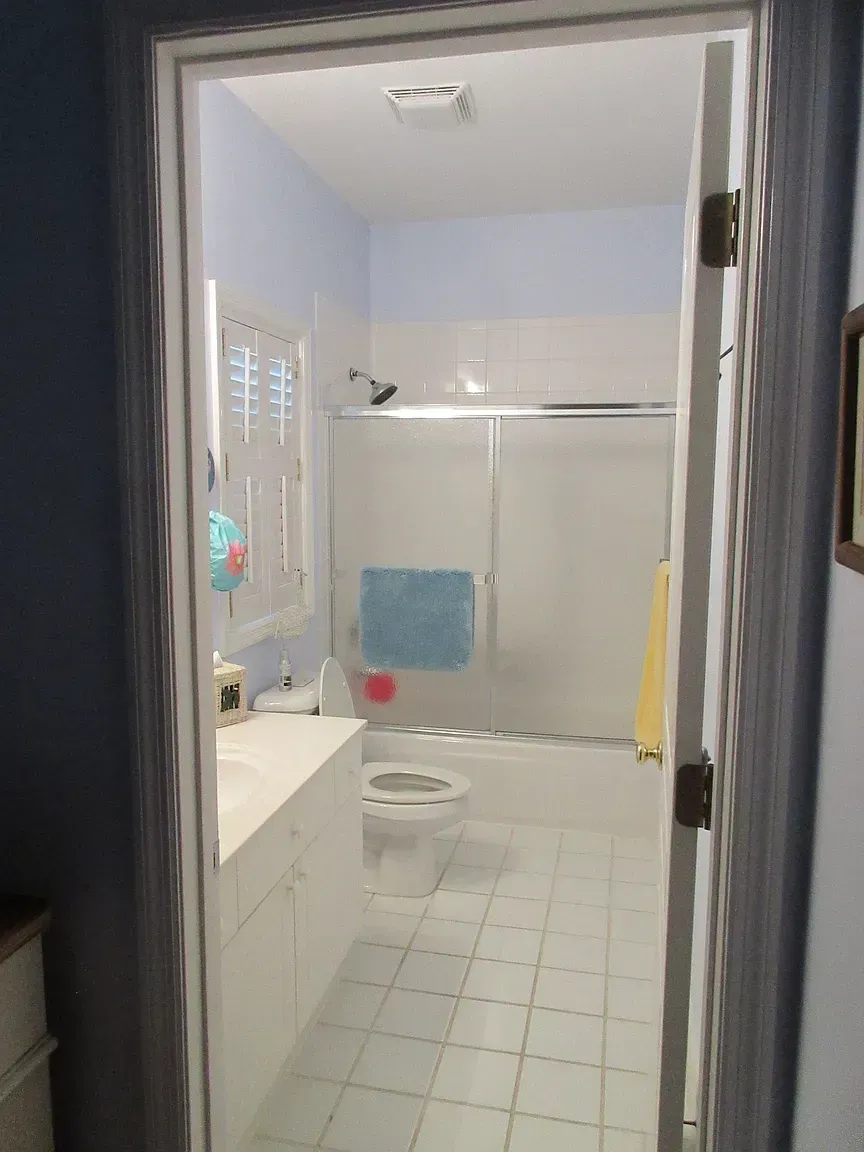 Bathroom interior, seen from doorway. White tile floor, blue walls, white shower/tub, toilet, and sink.