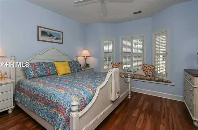 Bedroom with blue walls, white bed frame, bay window with shutters, and wood flooring.