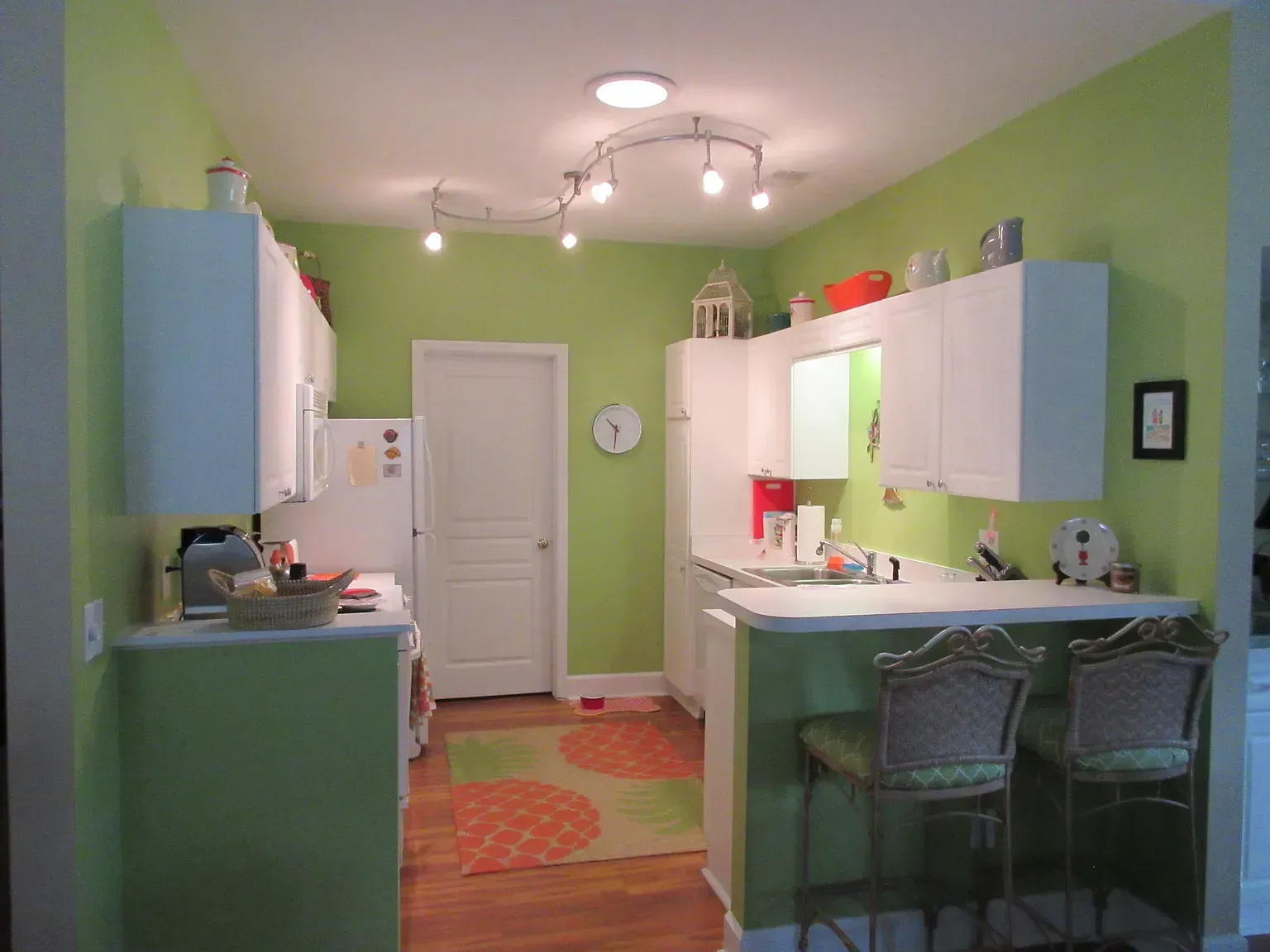 Bright green kitchen with white cabinets, breakfast bar, and track lighting.