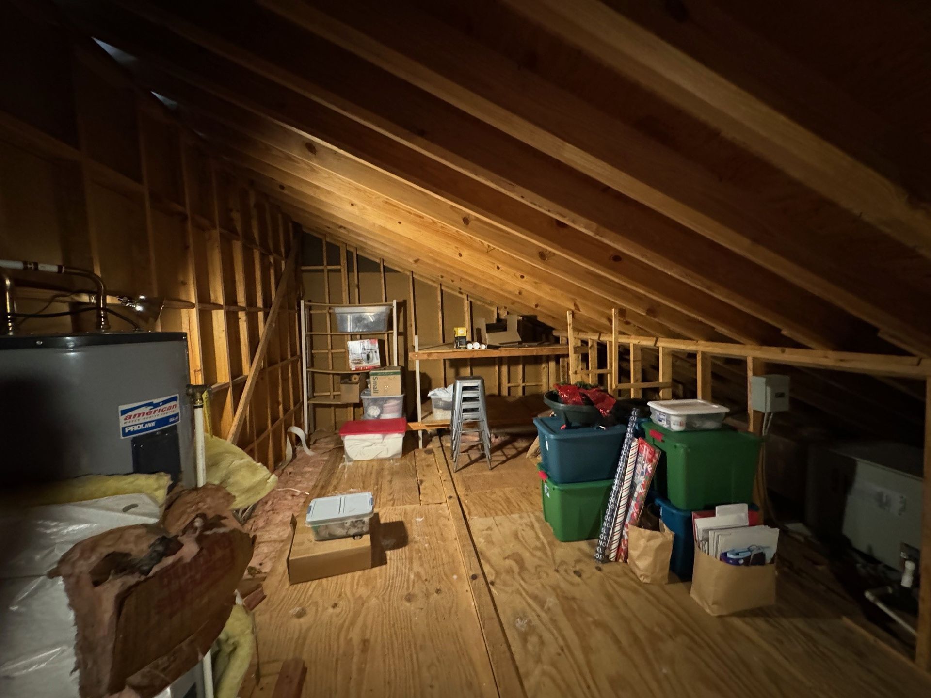 Attic storage space with exposed rafters, wooden floor, and boxes, bins, and furniture scattered around.