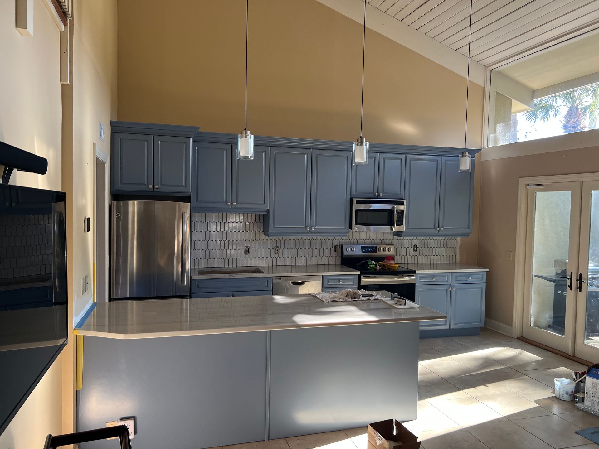 Blue kitchen with stainless steel appliances, light gray countertops, and pendant lights.