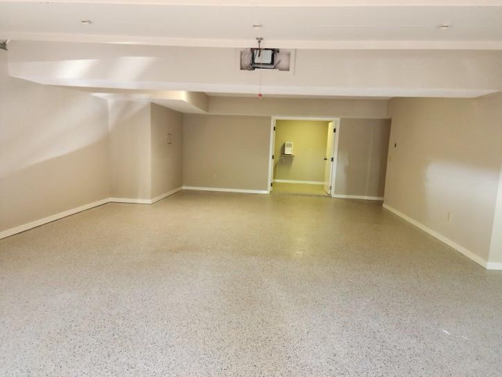 Empty room with speckled flooring and beige walls, doorway in the center, ceiling beams.