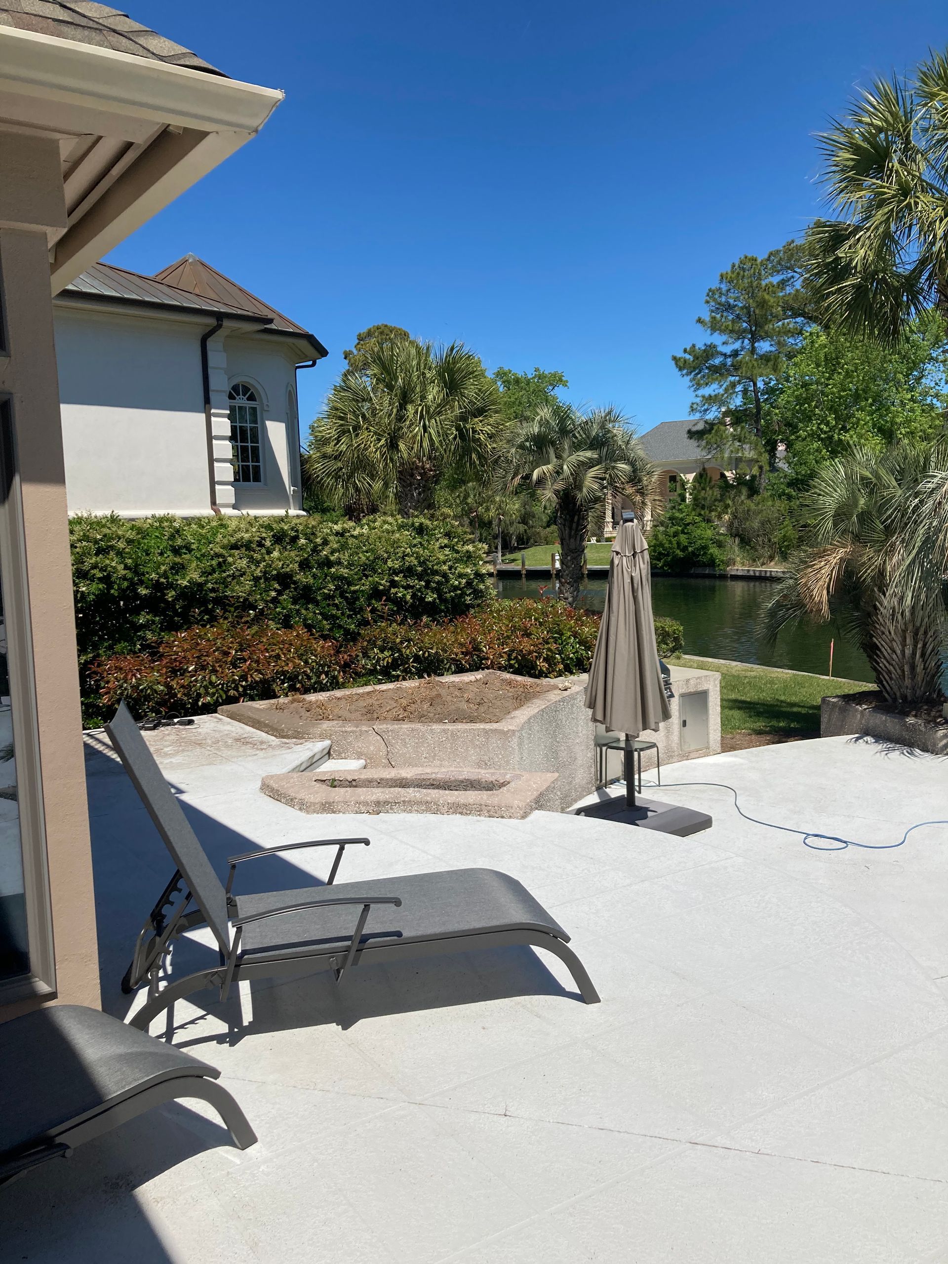 Patio with lounge chair, steps, and water view under a sunny, blue sky.