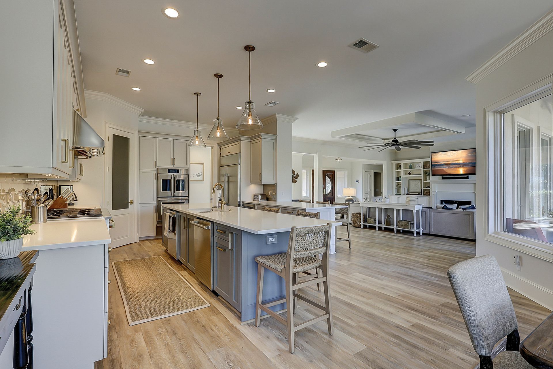 Spacious kitchen with a large island, stainless steel appliances, and wood flooring. Light fixtures hang above the island.