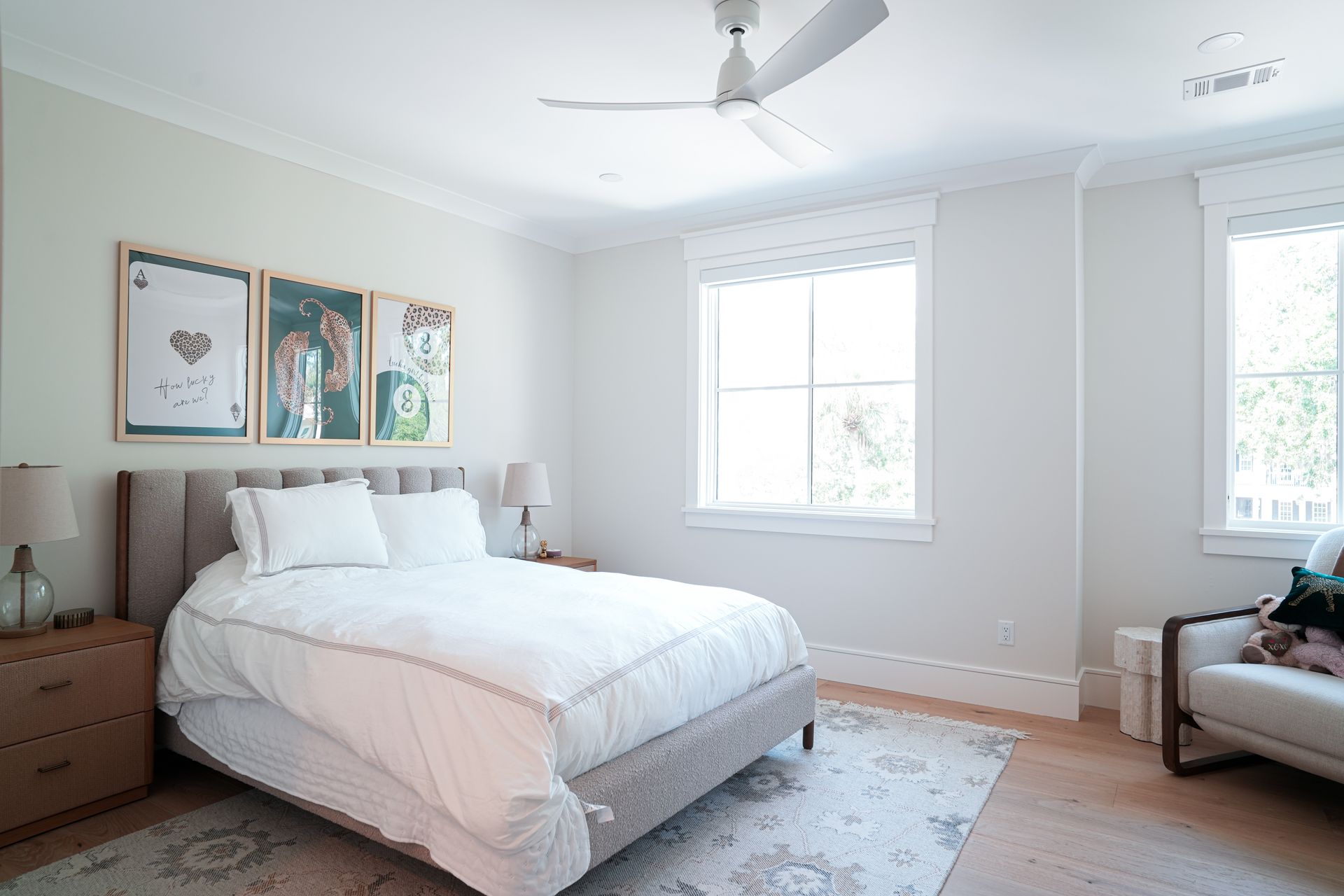 Bedroom with a bed, nightstand, and armchair, featuring artwork and a window.