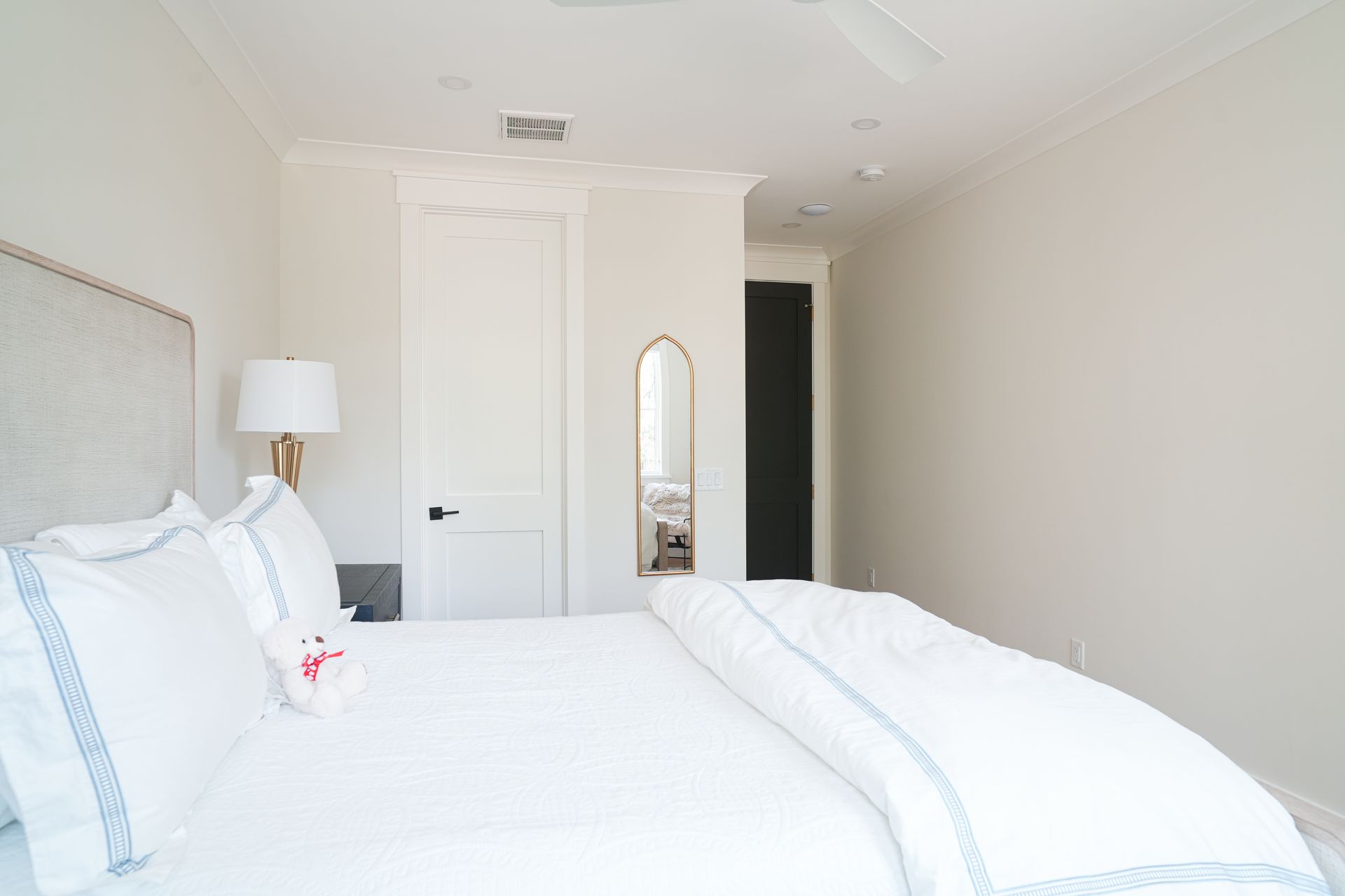 Bedroom with white bedding, headboard, lamp, and arched mirror.