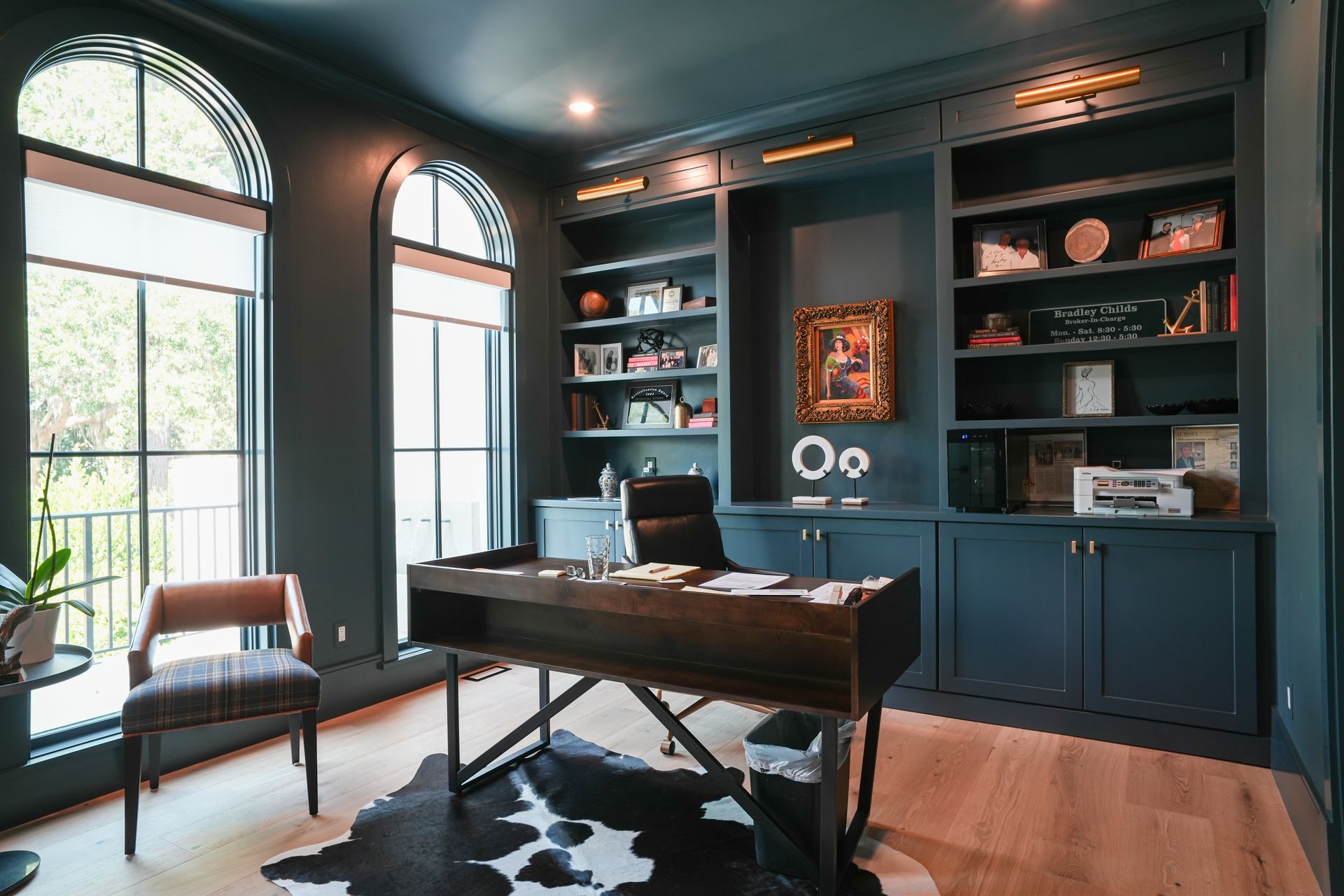 Office with dark blue walls, built-in shelving, arched windows, desk, cowhide rug, and leather chair.
