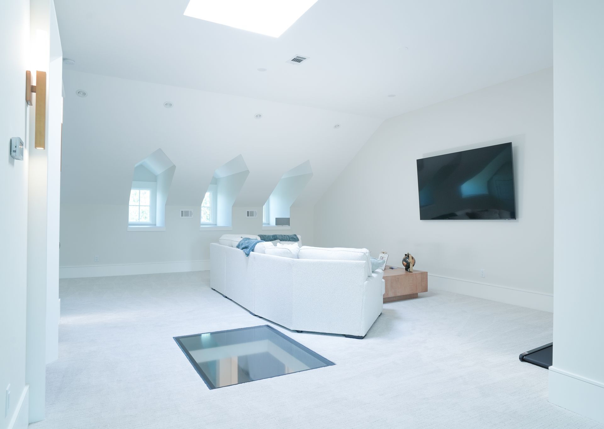 Bright, modern loft interior with a white sofa, TV, and skylight. Includes a glass floor feature.