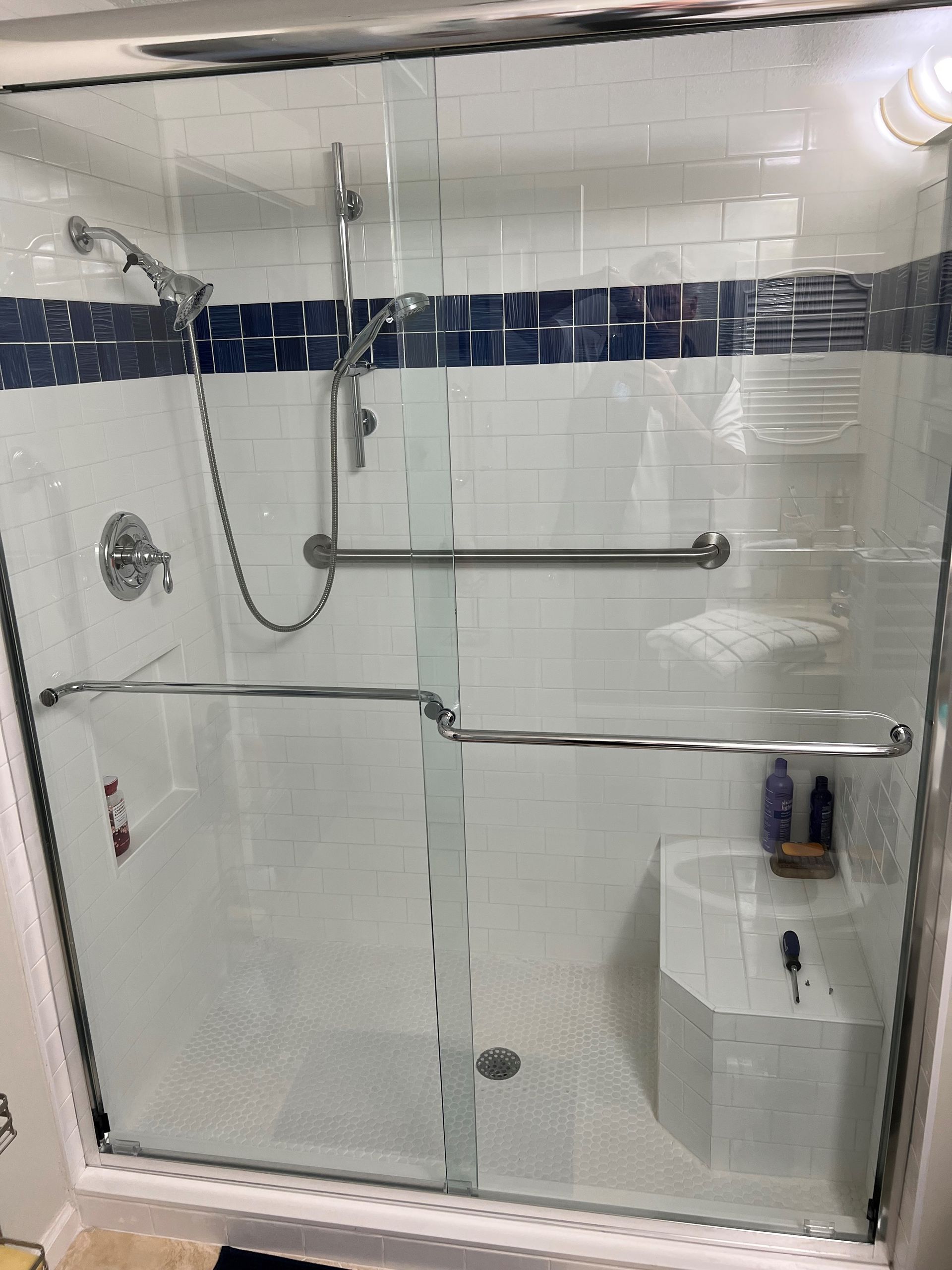 Shower with glass doors, white and blue tiled walls, and grab bars.