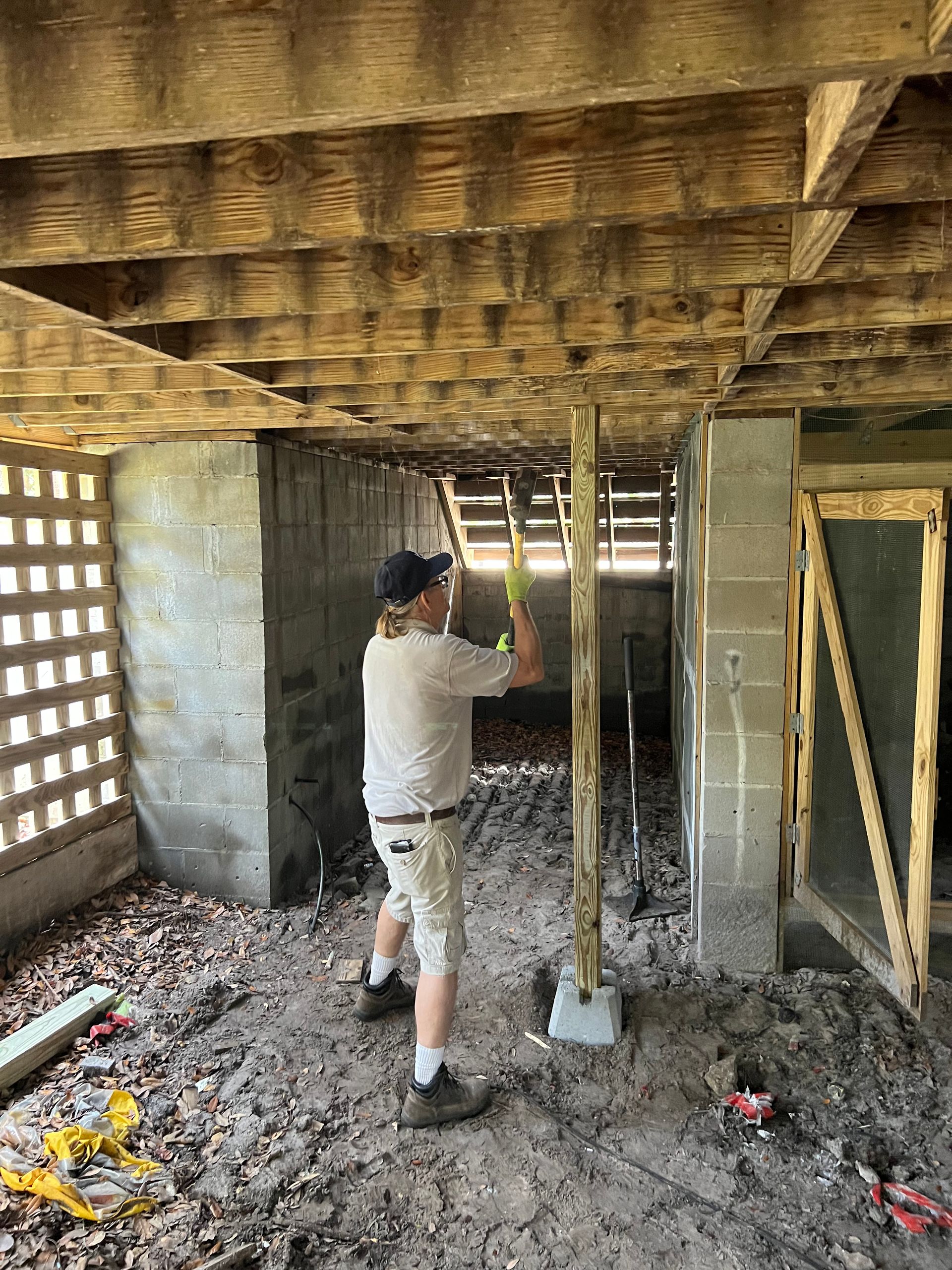 Person installing a support beam under a structure. They're working outdoors, and it appears they're working under a building.