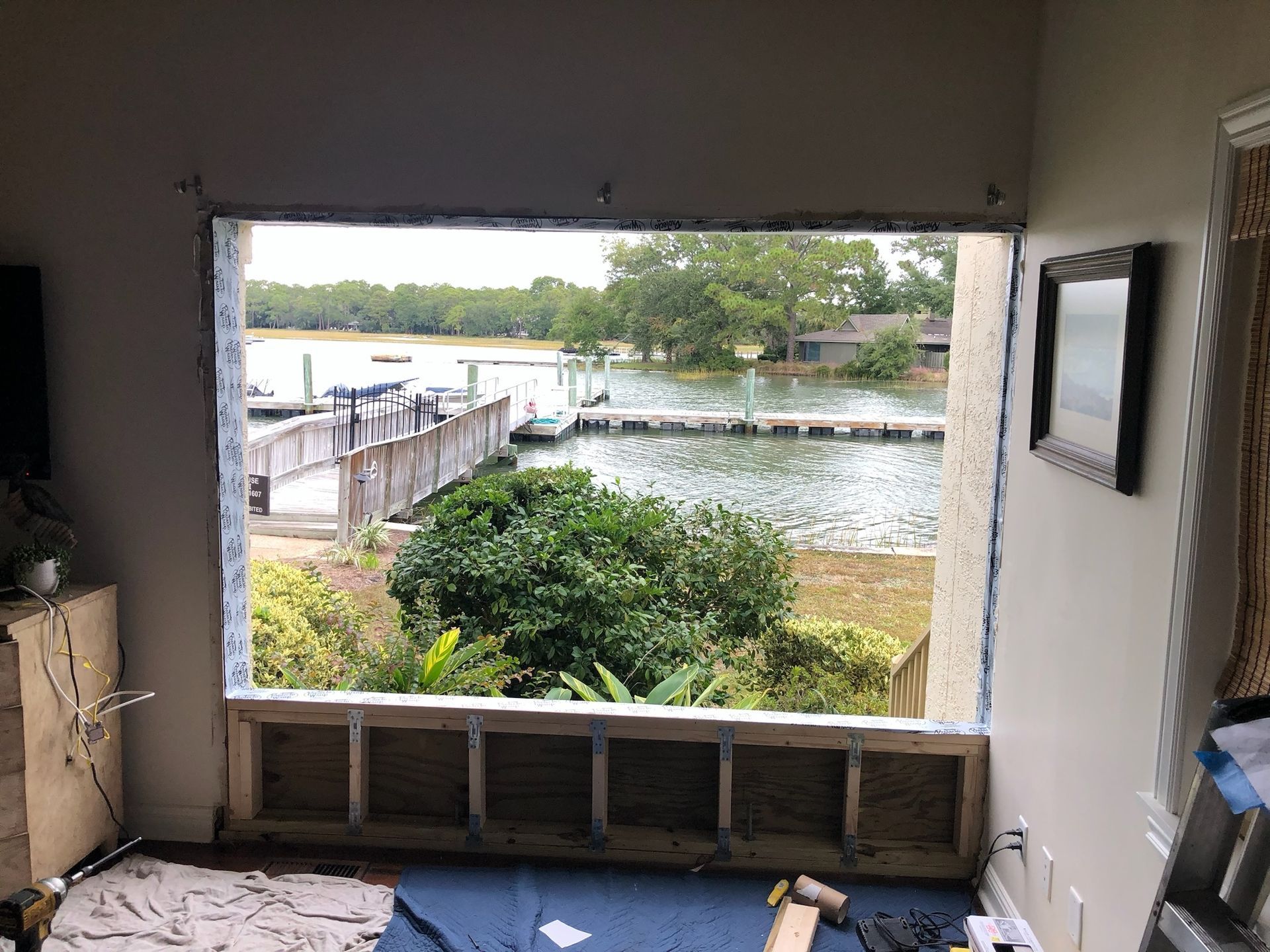 View from a window opening onto a waterfront dock. Window frame is unfinished with construction underway.