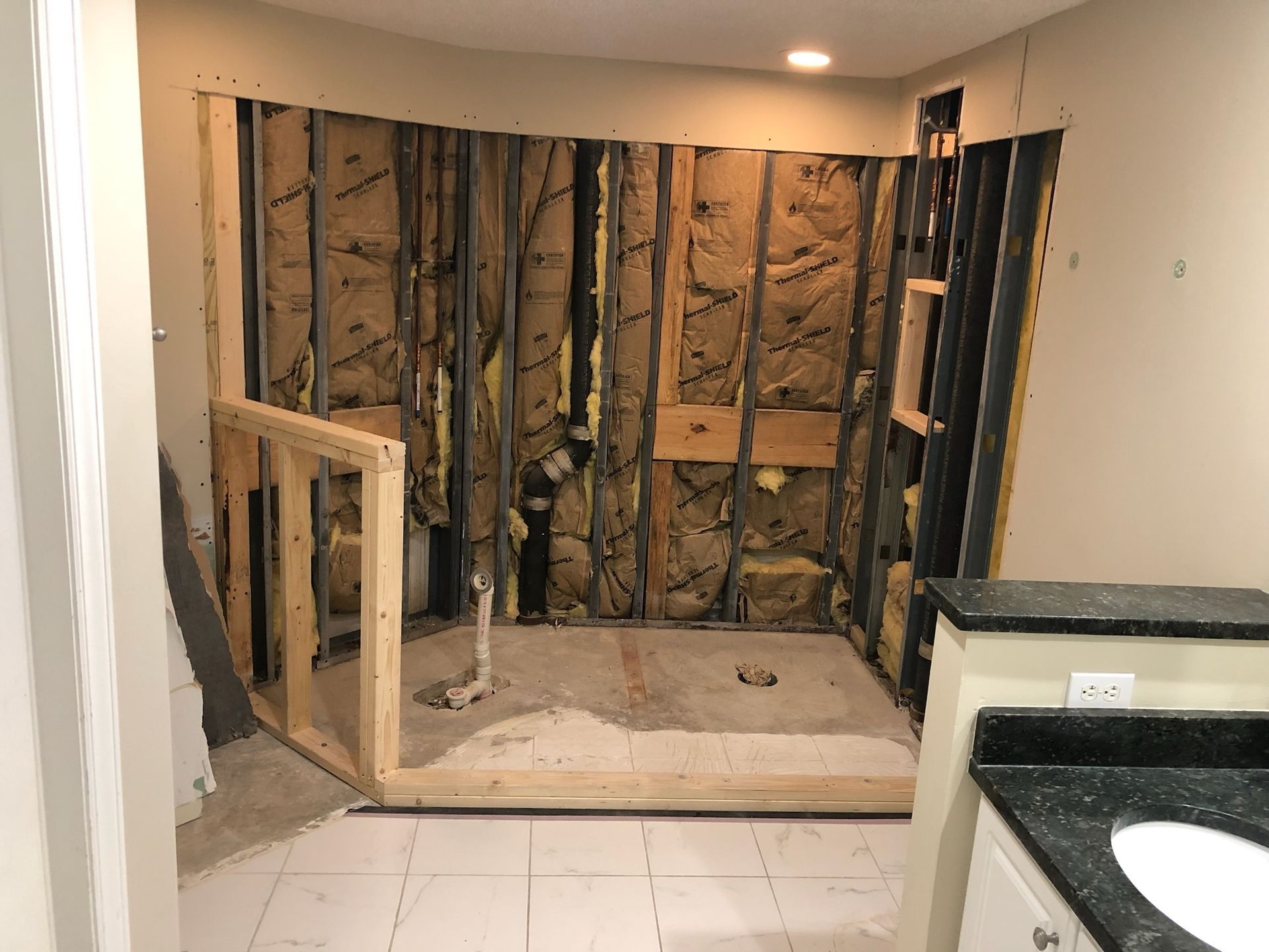 Bathroom renovation in progress, framing and insulation exposed, tile floor, vanity on the right.