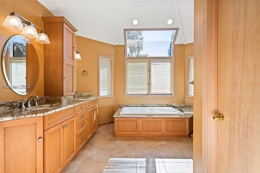 6 Planters - Before: Bathroom with wood cabinets, oval mirror, and a built-in tub under a large window.
