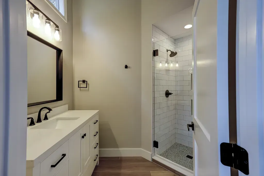 6 Planters - After: Bathroom interior with white vanity, framed mirror, glass shower, and wood-look flooring.