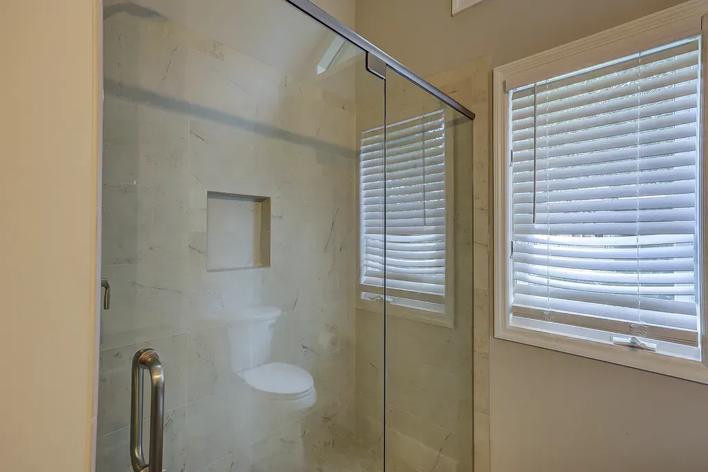 6 Planters - After: Glass shower with sliding door and window with blinds in a bathroom.