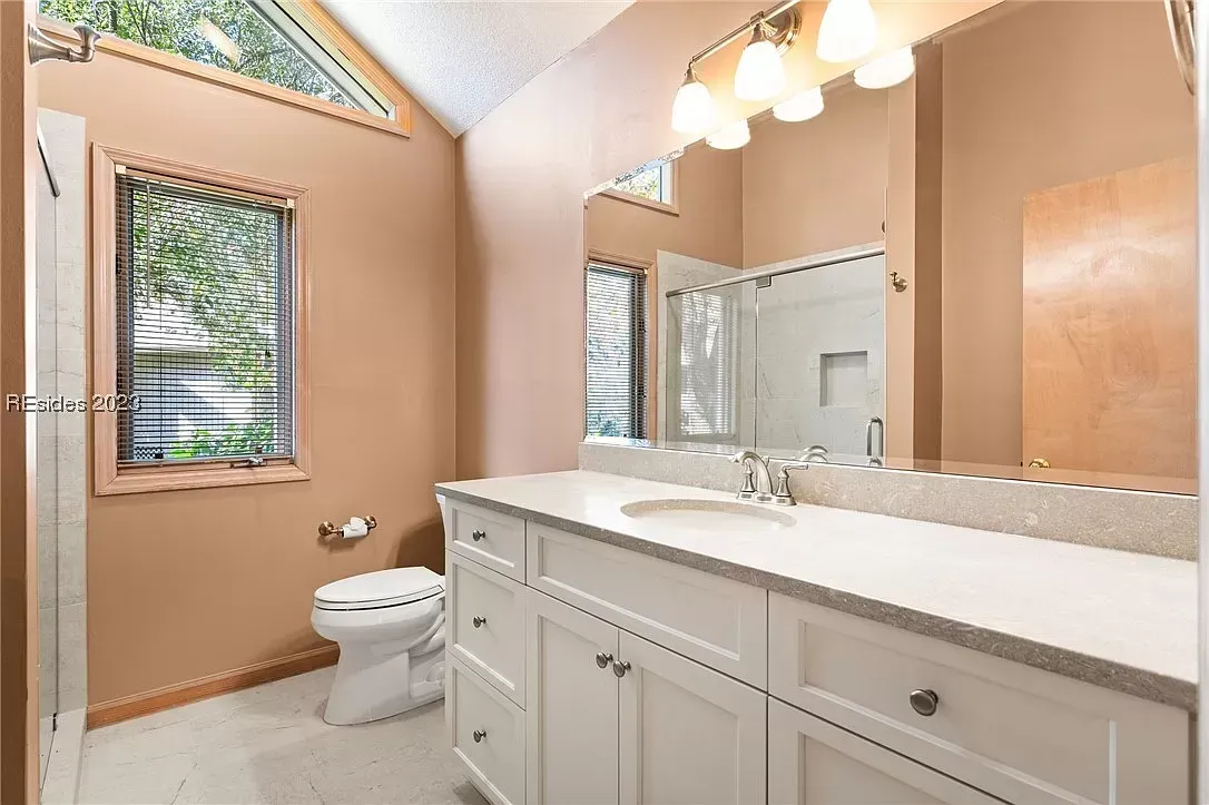 6 Planters - Before: Bathroom with white vanity, toilet, large mirror, and angled windows; tan walls.