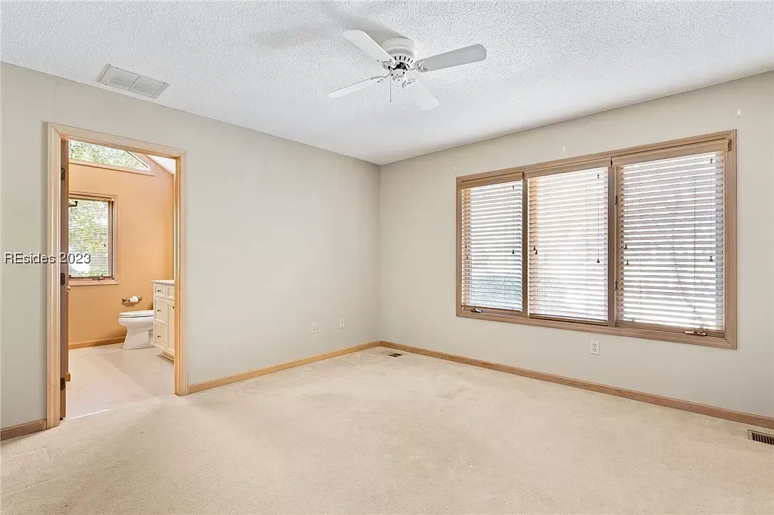 6 Planters - Before: Empty bedroom with beige walls, carpet, and a bathroom doorway; a window with blinds is on the right.