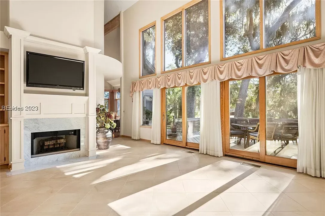 6 Planters - Before: Spacious living room with fireplace, TV, and large windows overlooking a deck and trees.