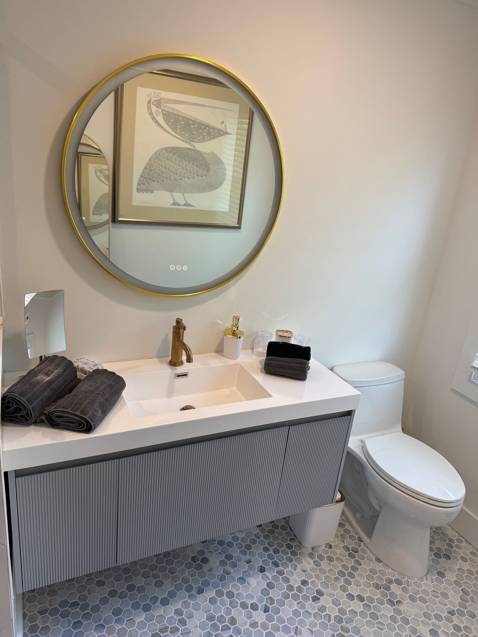 (18 Ensis) Port Royal Full Home Renovation: Bathroom with a floating vanity, gold-framed mirror, and patterned floor.