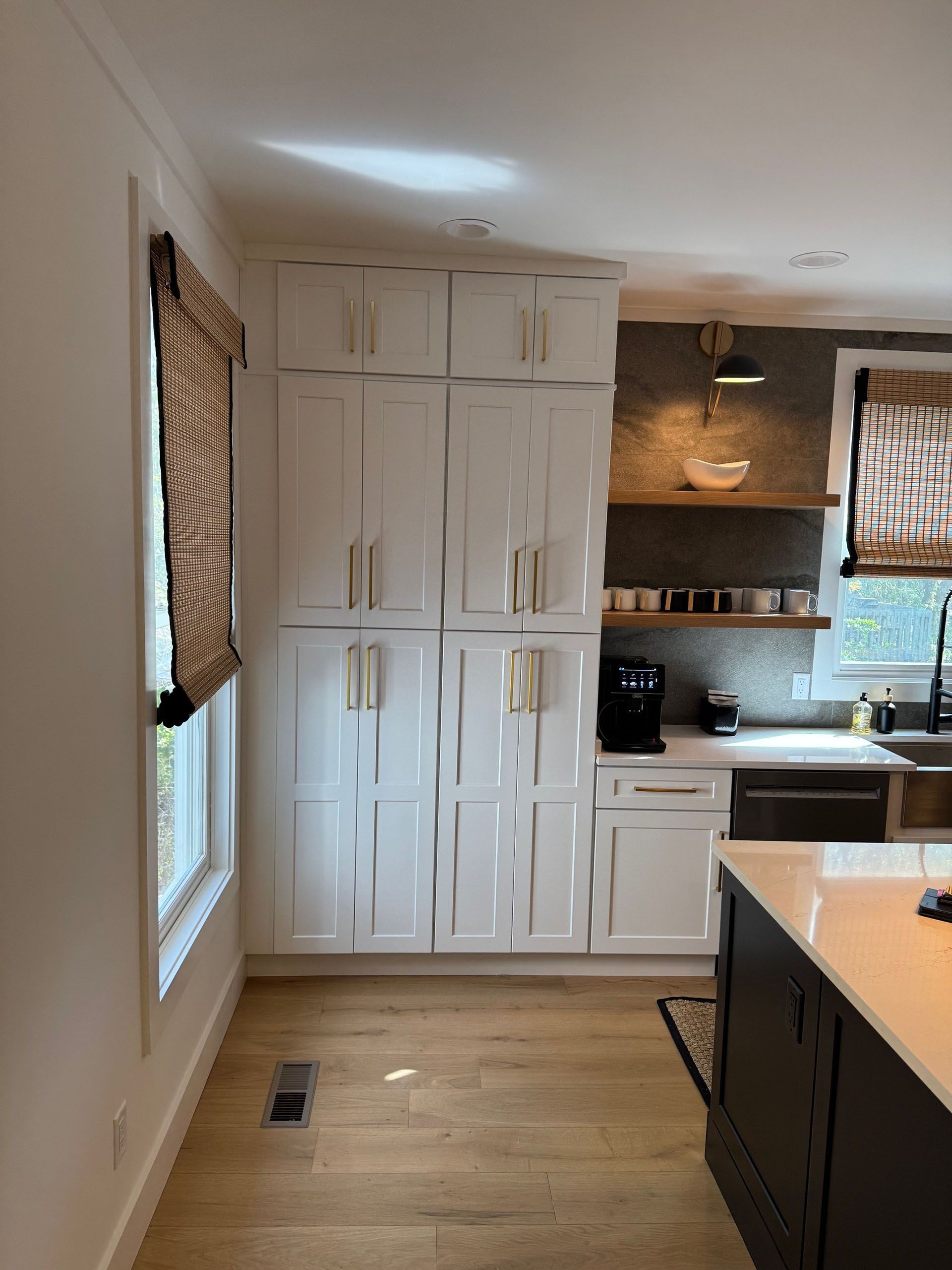 (18 Ensis) Port Royal Full Home Renovation: White kitchen with tall cabinets, light wood floor, and black countertops.