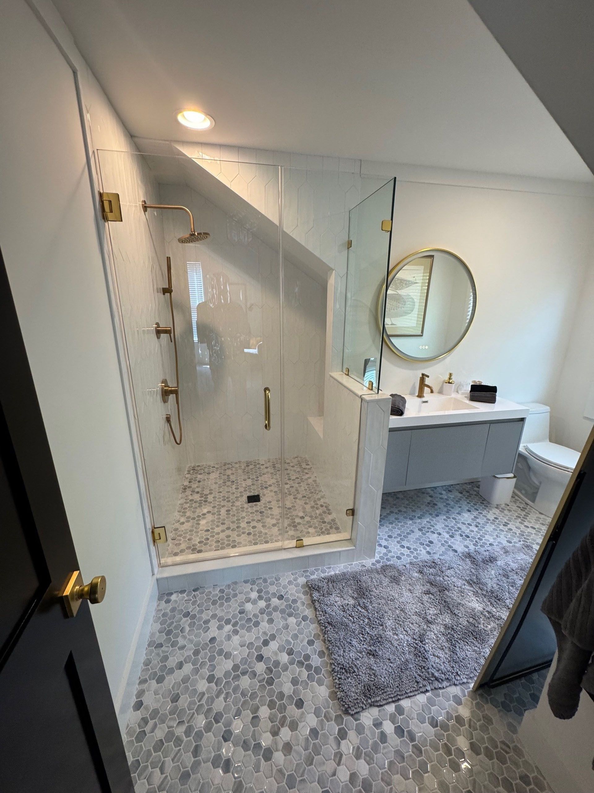 (18 Ensis) Port Royal Full Home Renovation: Bathroom with glass shower, white walls, gray vanity, round mirror, and patterned floor.