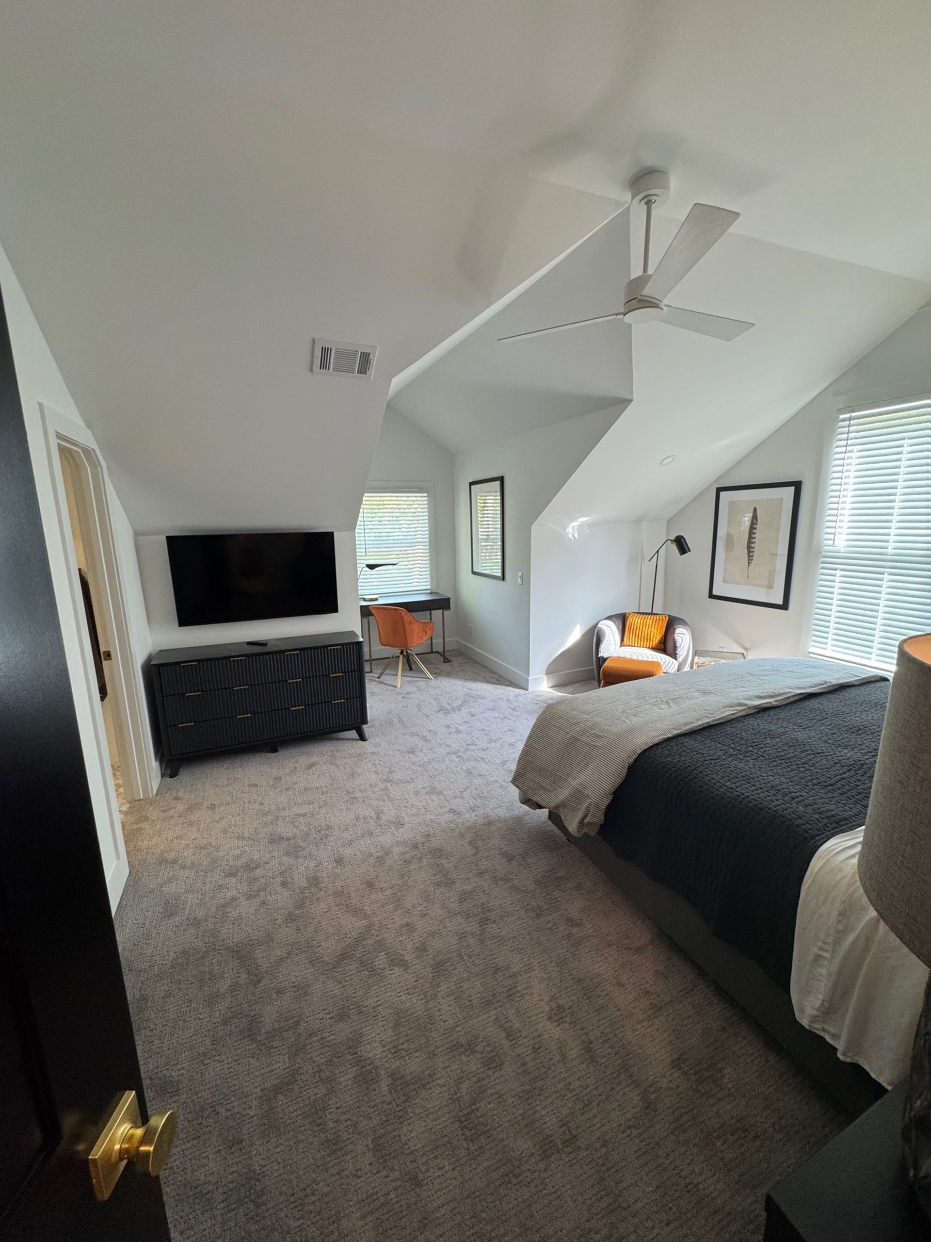 (18 Ensis) Port Royal Full Home Renovation: Bedroom with angled ceiling, gray carpet, black dresser, TV, bed, chair, and desk.