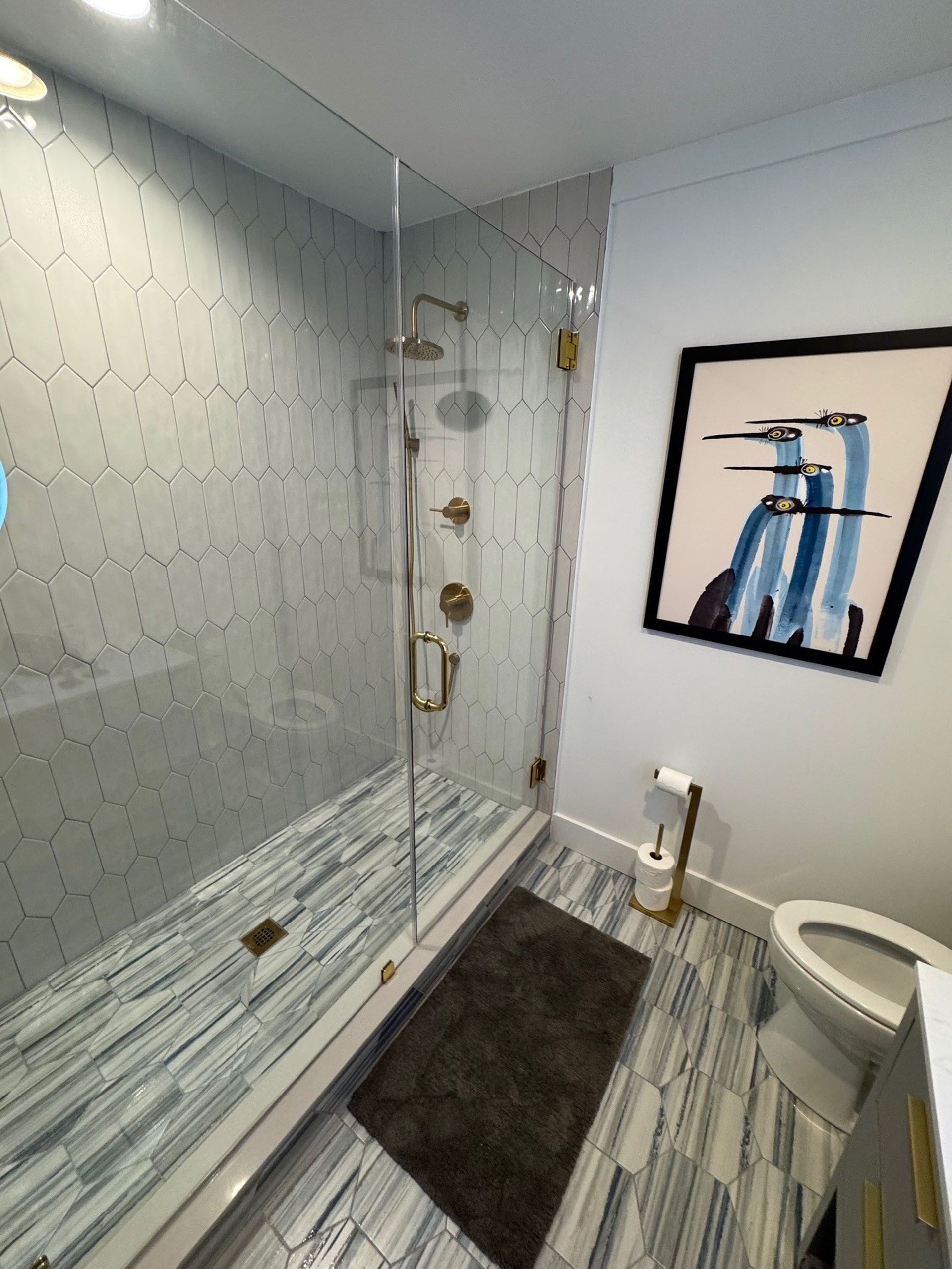 (18 Ensis) Port Royal Full Home Renovation: Bathroom with tiled floor and shower, gold fixtures, artwork, and toilet.