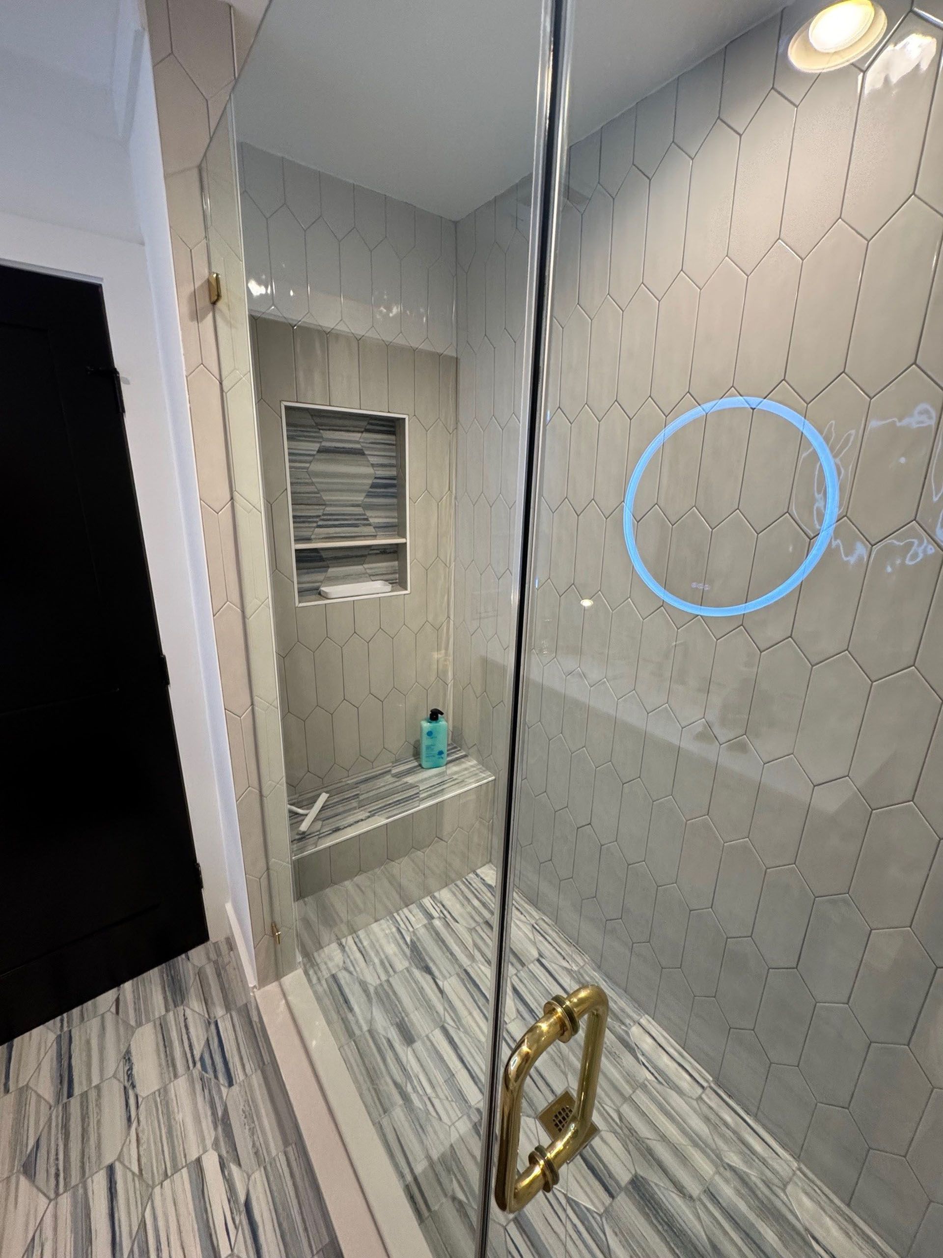 (18 Ensis) Port Royal Full Home Renovation: Shower with glass door, gray hexagonal tiles, a built-in bench, and a blue shampoo bottle.