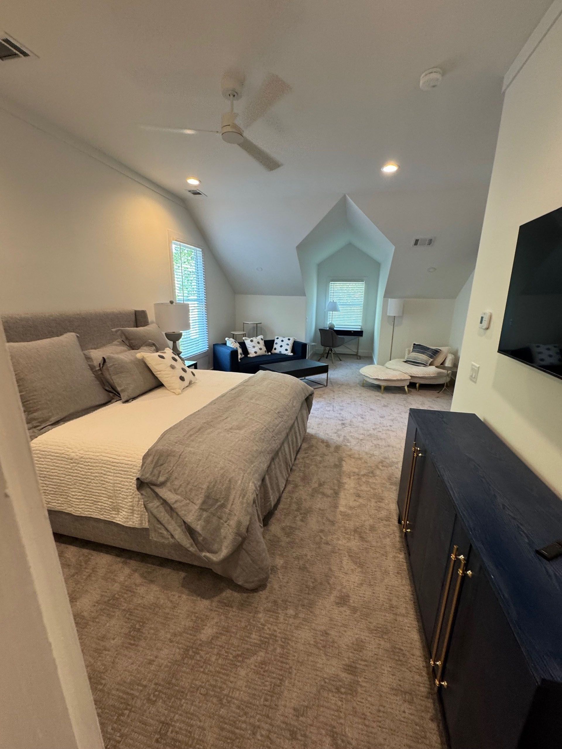 (18 Ensis) Port Royal Full Home Renovation: Spacious bedroom with a bed, dresser, and seating area under a vaulted ceiling. Neutral tones.
