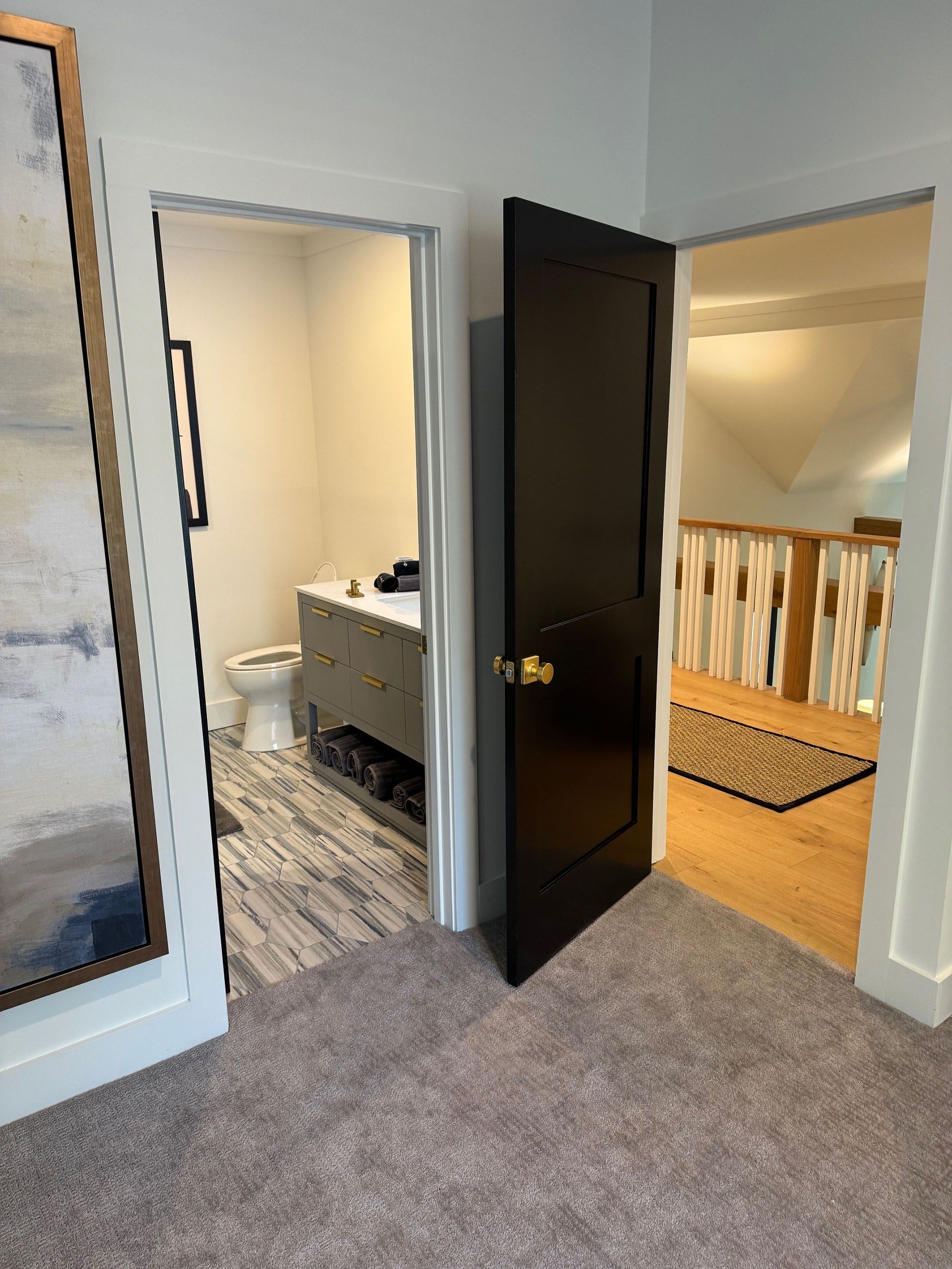Bedroom with three open doorways: bathroom, hallway with stairs, and black door.