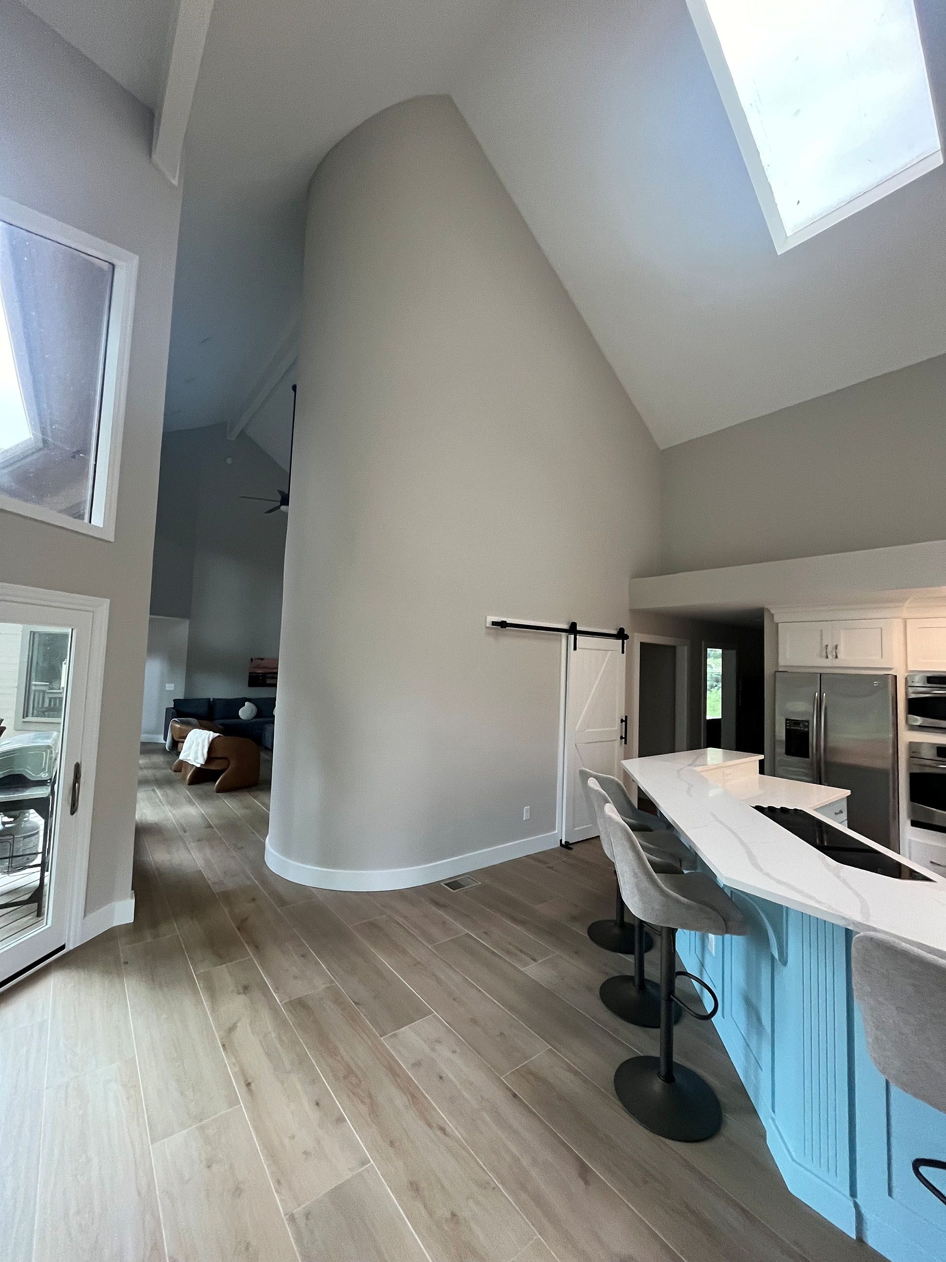 6 Planters - After: Light-filled modern kitchen with light wood floor and curved wall. Kitchen island with white countertop and blue base.