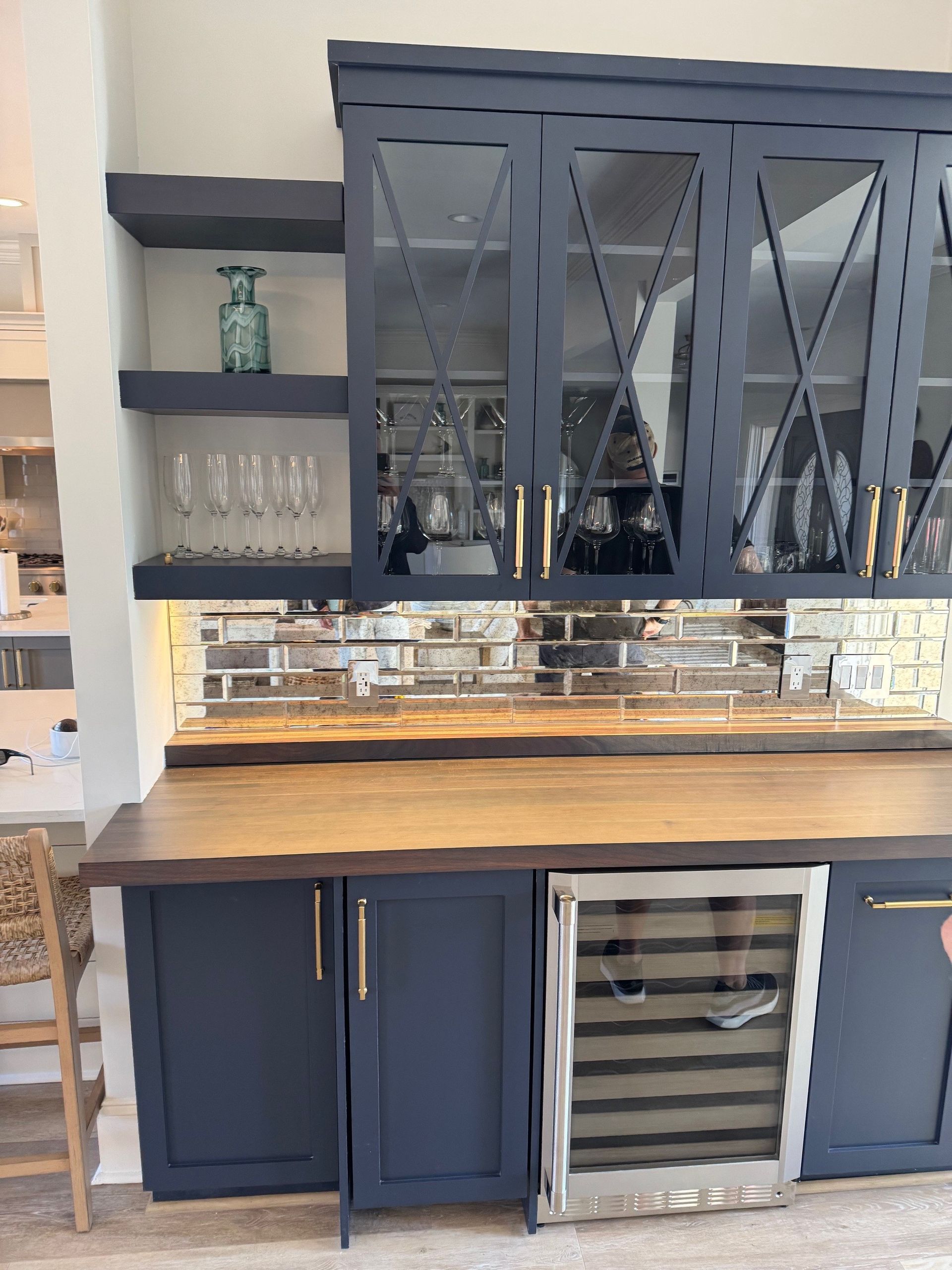 Navy blue bar with glass-front cabinets, wine fridge, and wooden countertop with a mirrored backsplash.