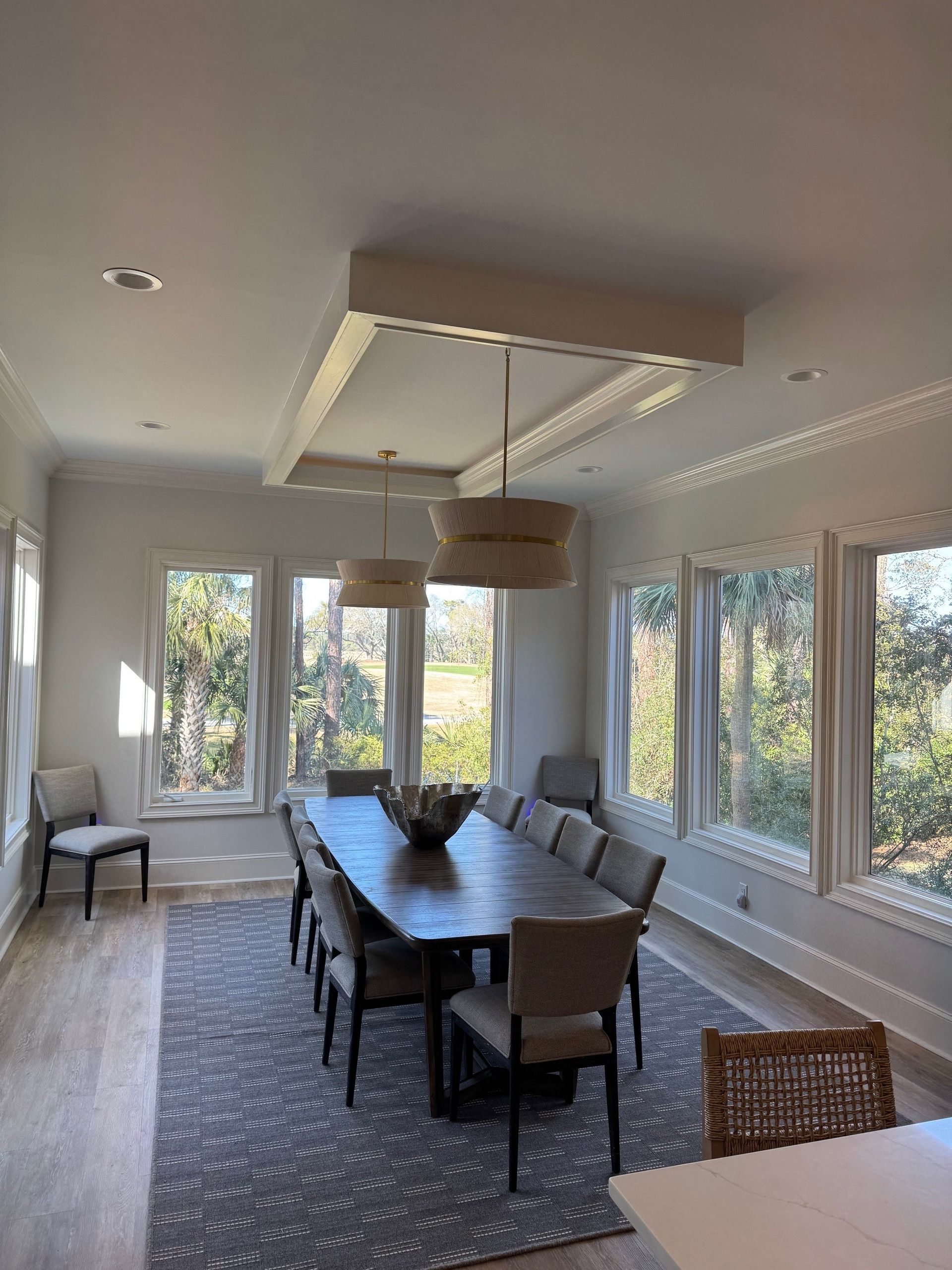 Dining room with long table, chairs, rug, and large windows.  Neutral colors and modern design.