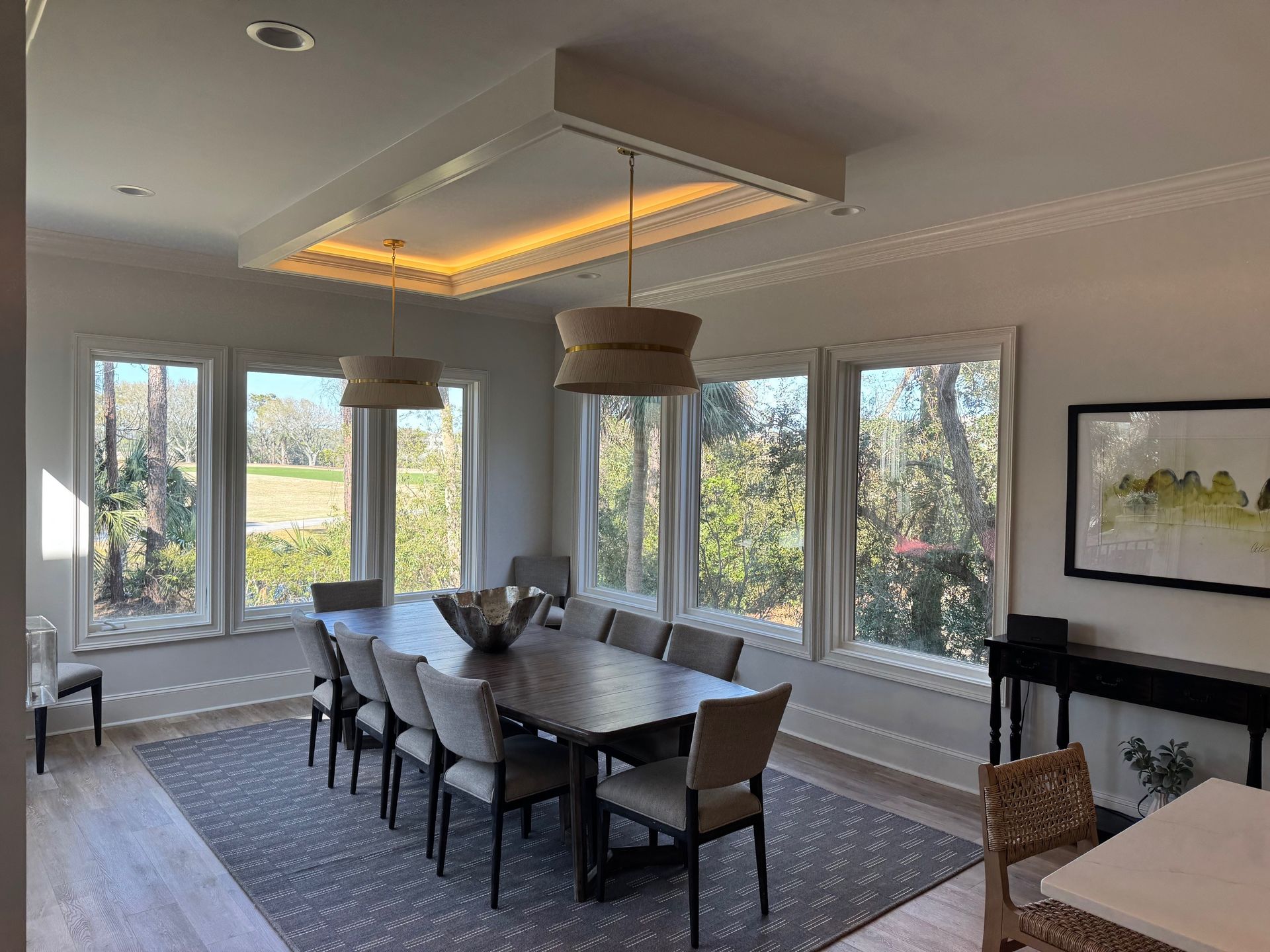 Dining room with long table, chairs, large windows, and decorative lighting.