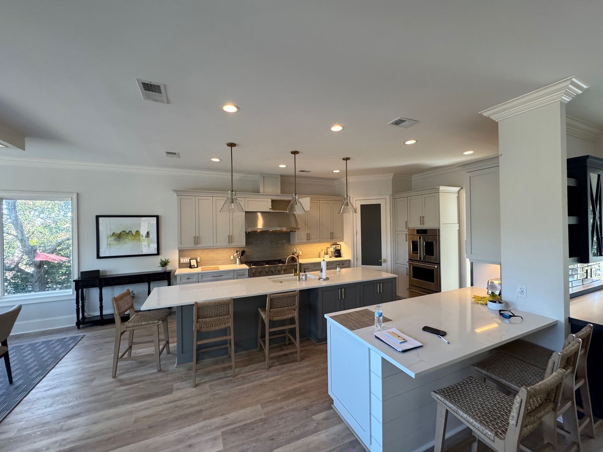 Spacious kitchen with two islands, light wood floor, gray and white cabinets, and bar stools.