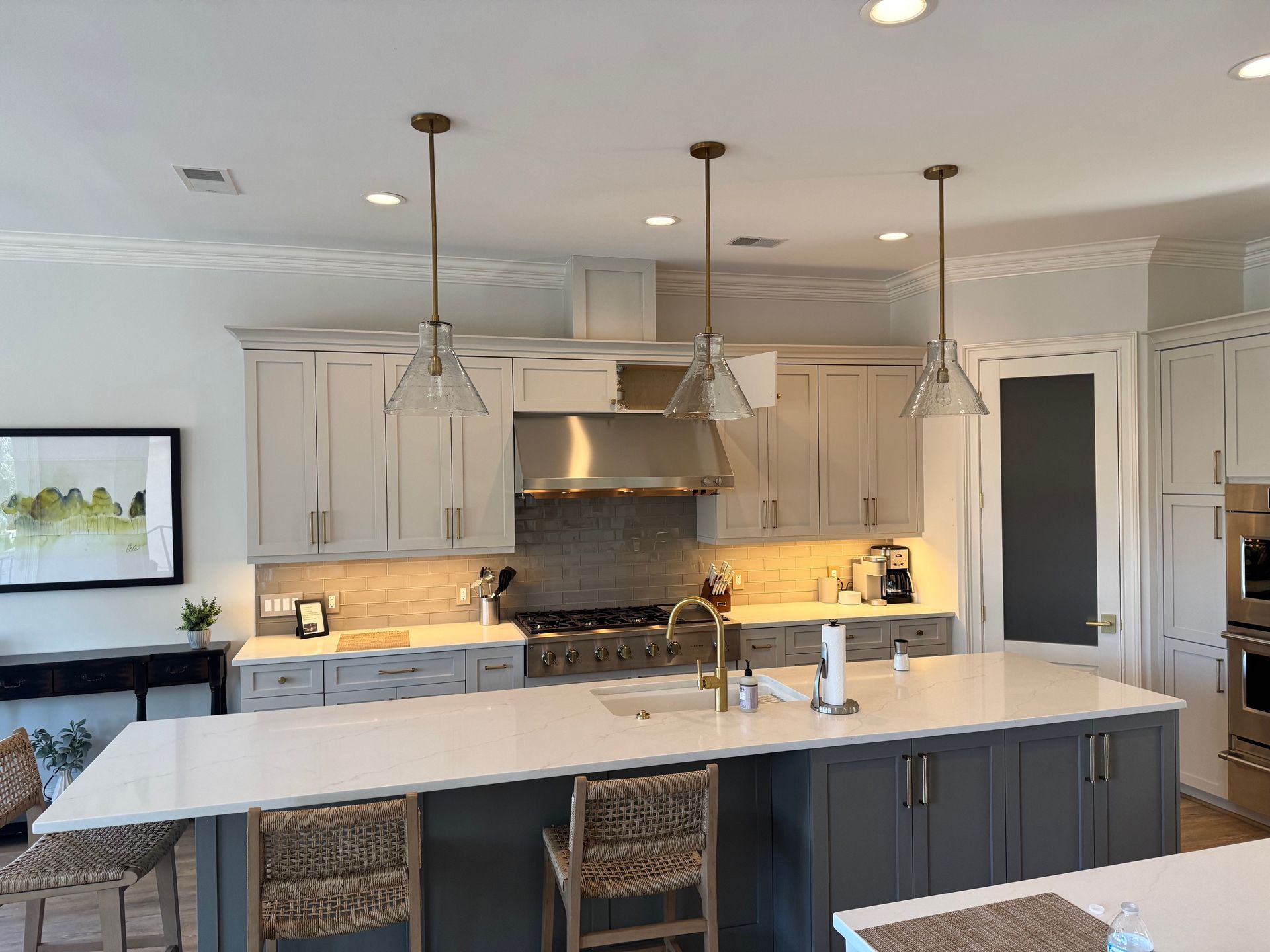 Modern kitchen with gray and white cabinets, island, three pendant lights, stainless steel appliances.